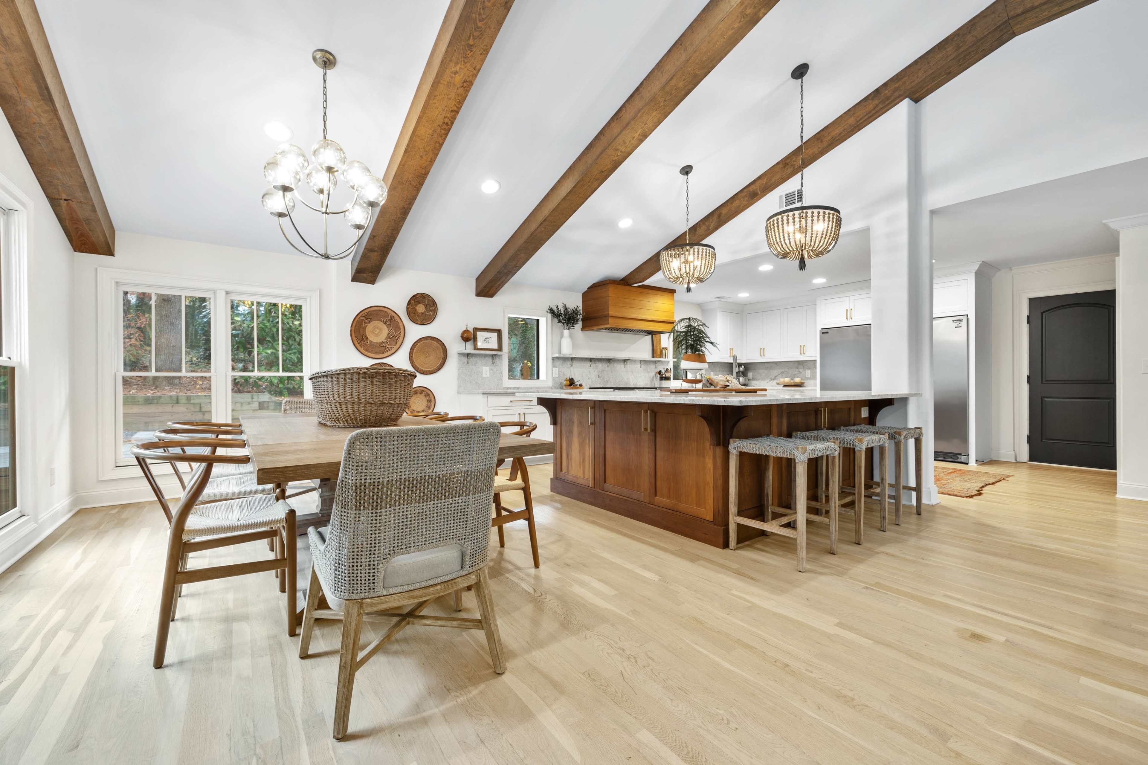 A modern kitchen and dining area features wooden beams, a large island with bar stools, a dining table, and various decorative elements on the walls.