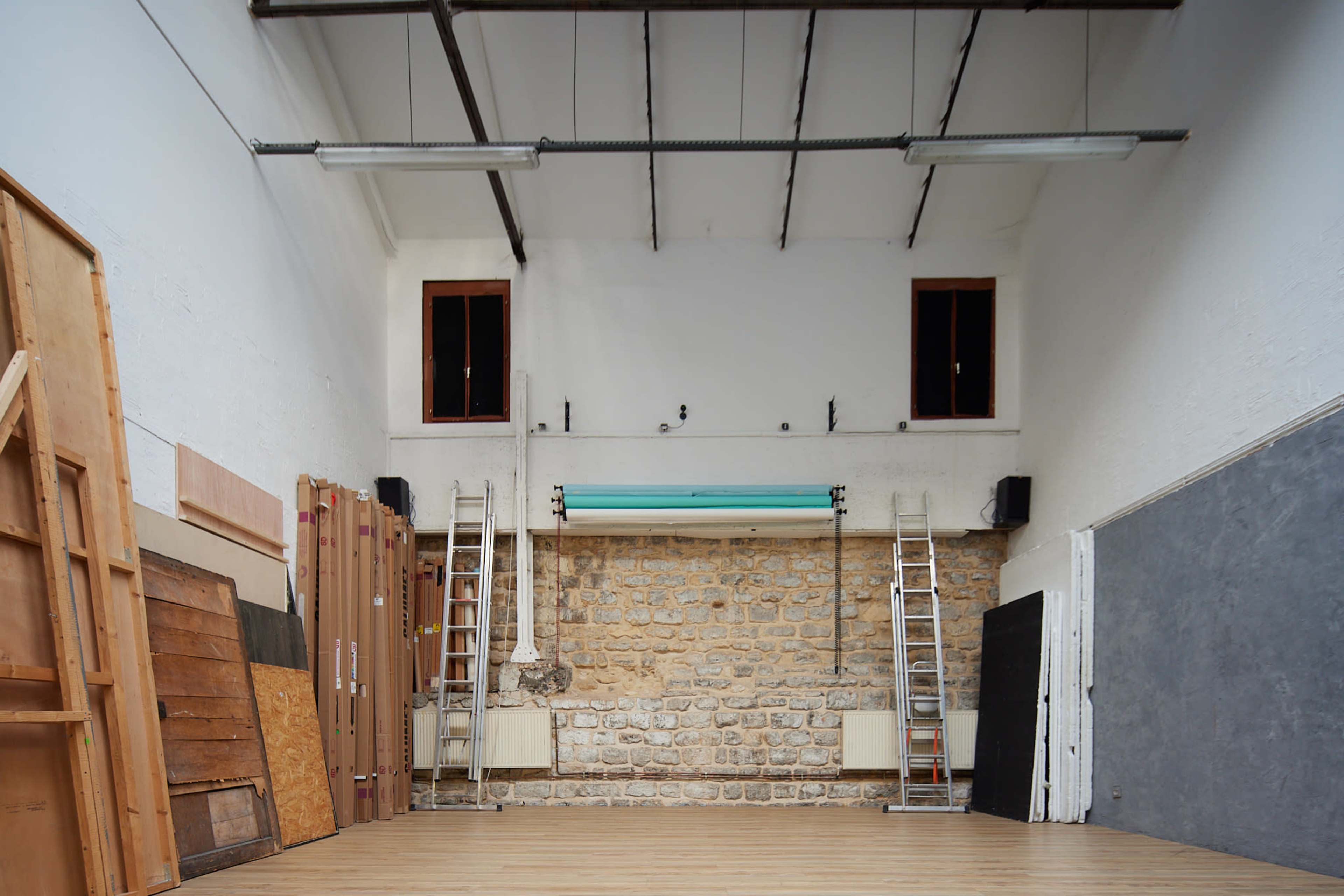 A spacious, empty room with wooden flooring, stone walls, and two ladders positioned against the back wall.