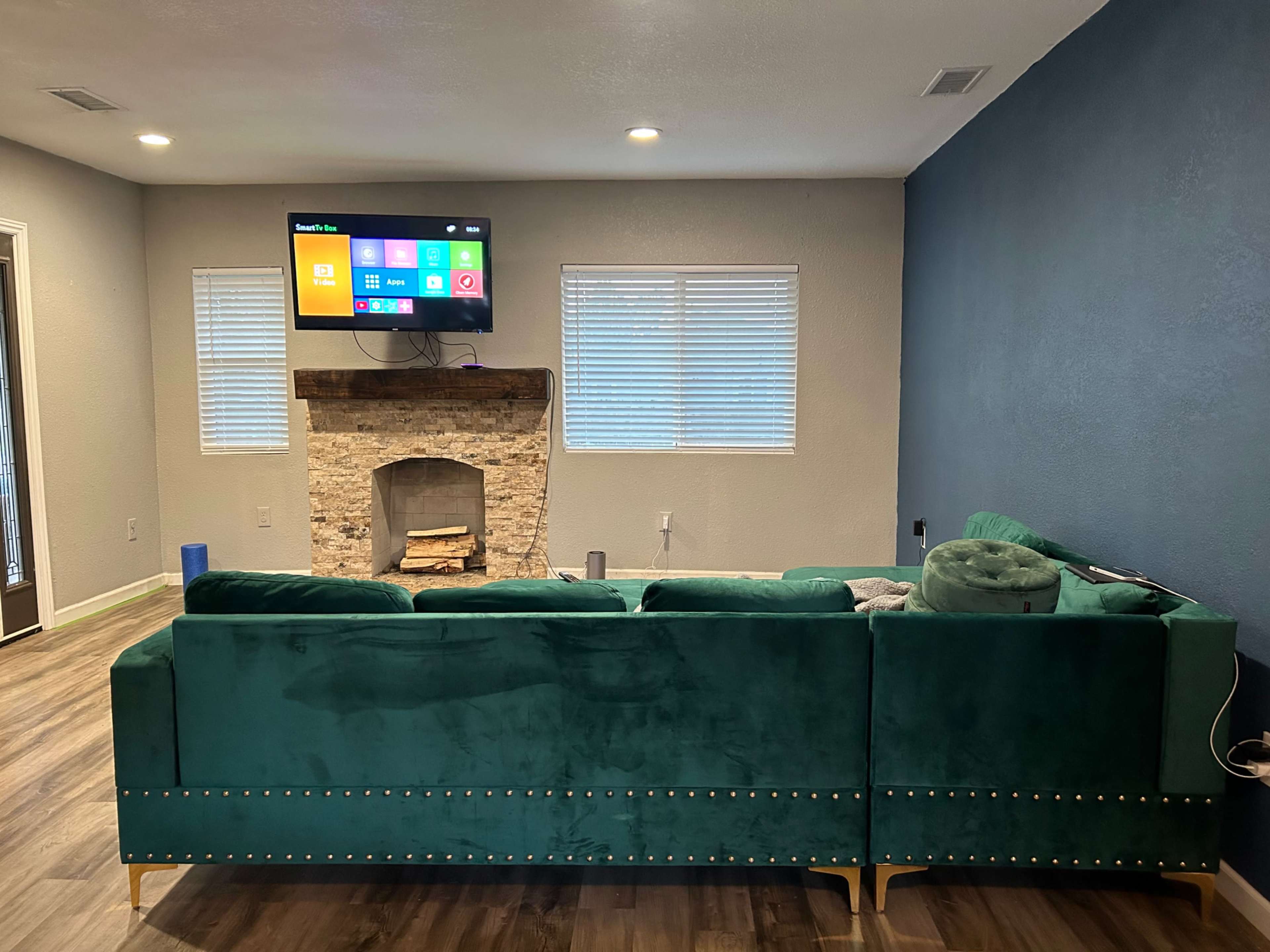 A living room with a green velvet sectional sofa facing a mounted television above a stone fireplace.