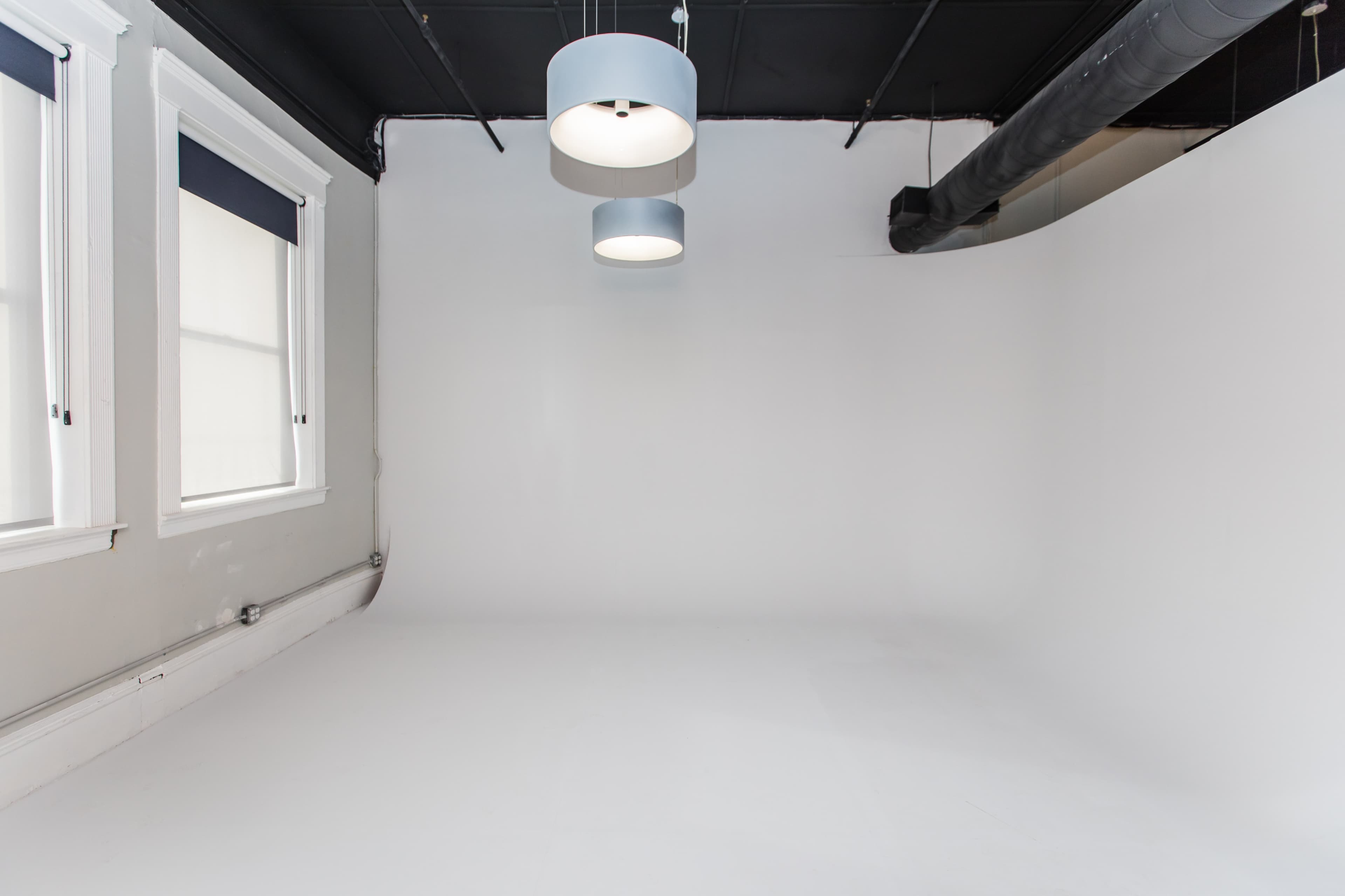 A spacious room with white walls and a simple ceiling featuring three pendant lights.