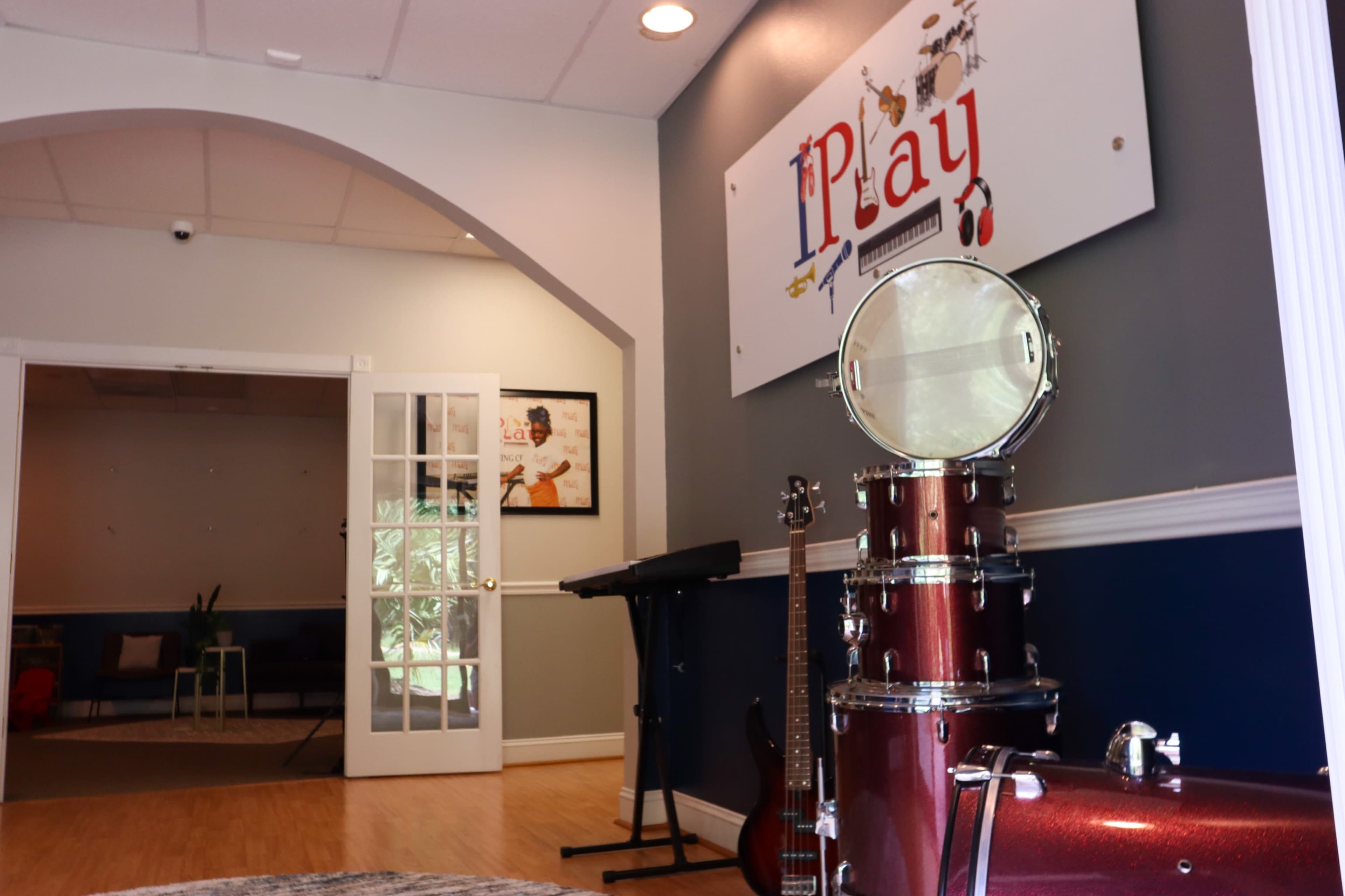 The image shows an interior space with musical instruments, including a drum set and guitar, and a sign that reads "iPlay" on the wall.