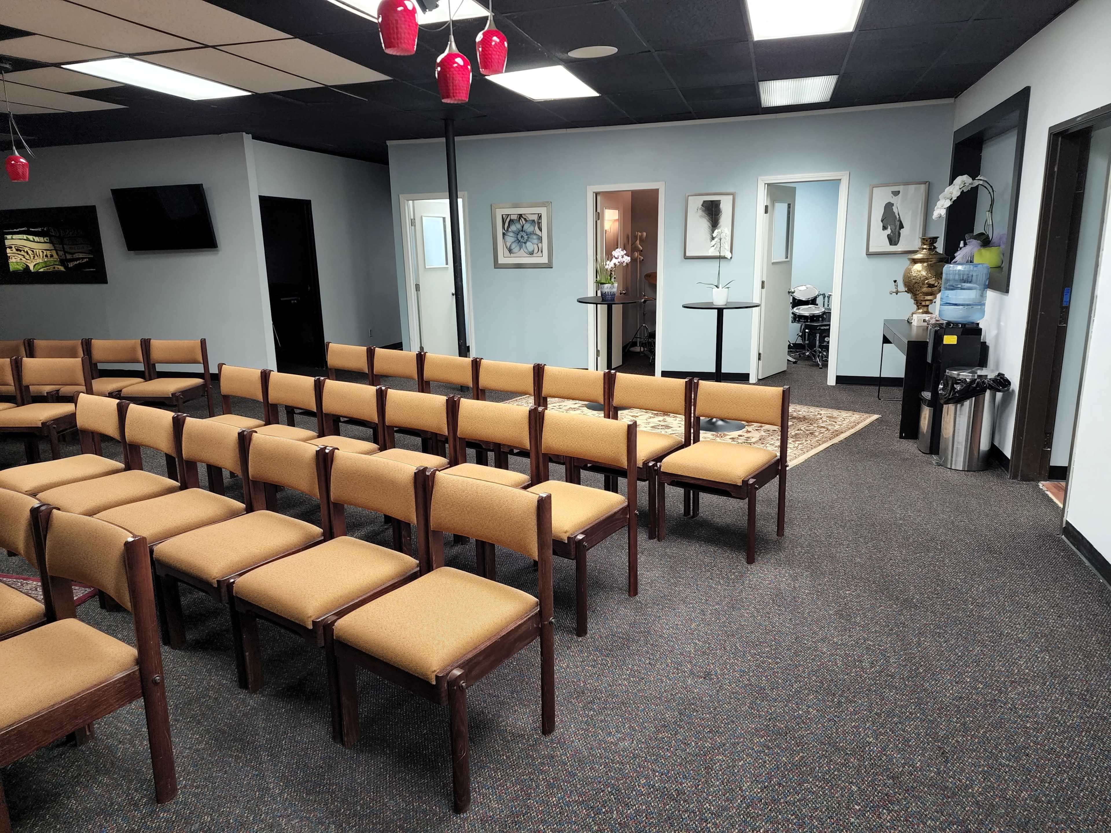 A waiting area with rows of wooden chairs facing a wall, leading to doorways that open into other rooms.