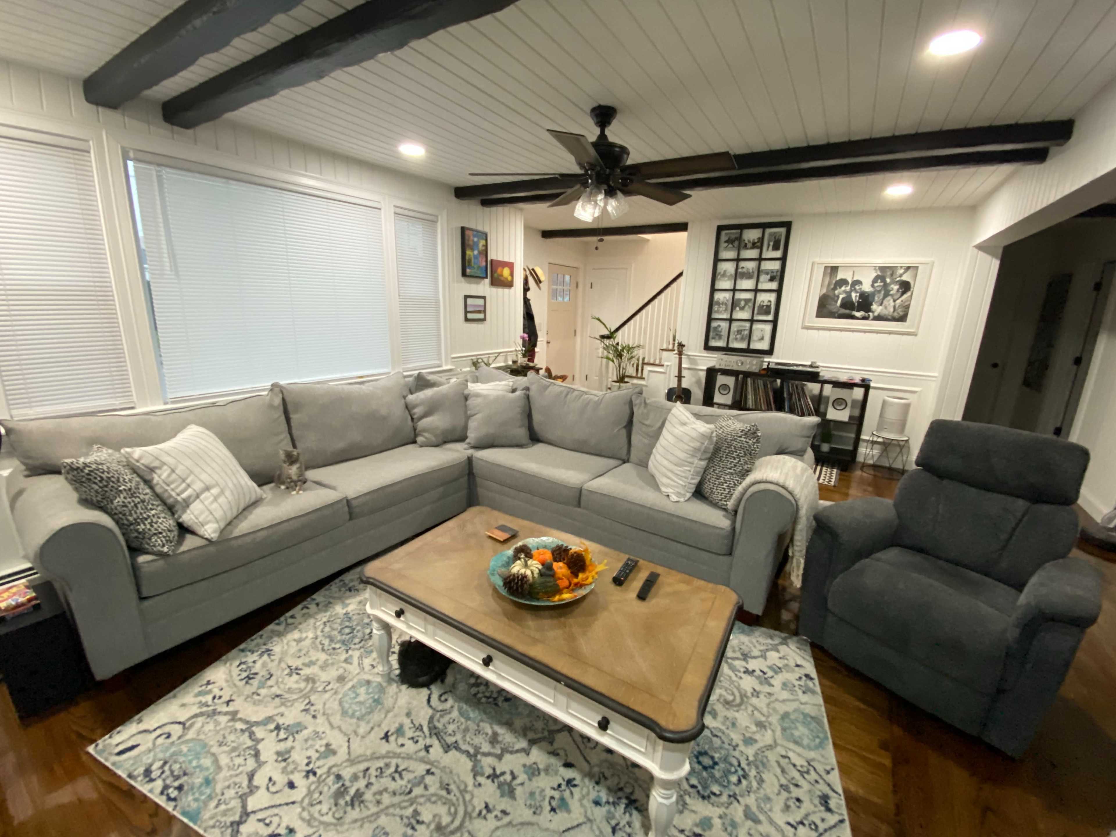 A living room with a gray sectional sofa, a wooden coffee table, and a recliner chair, all arranged around an area rug on polished hardwood floors.