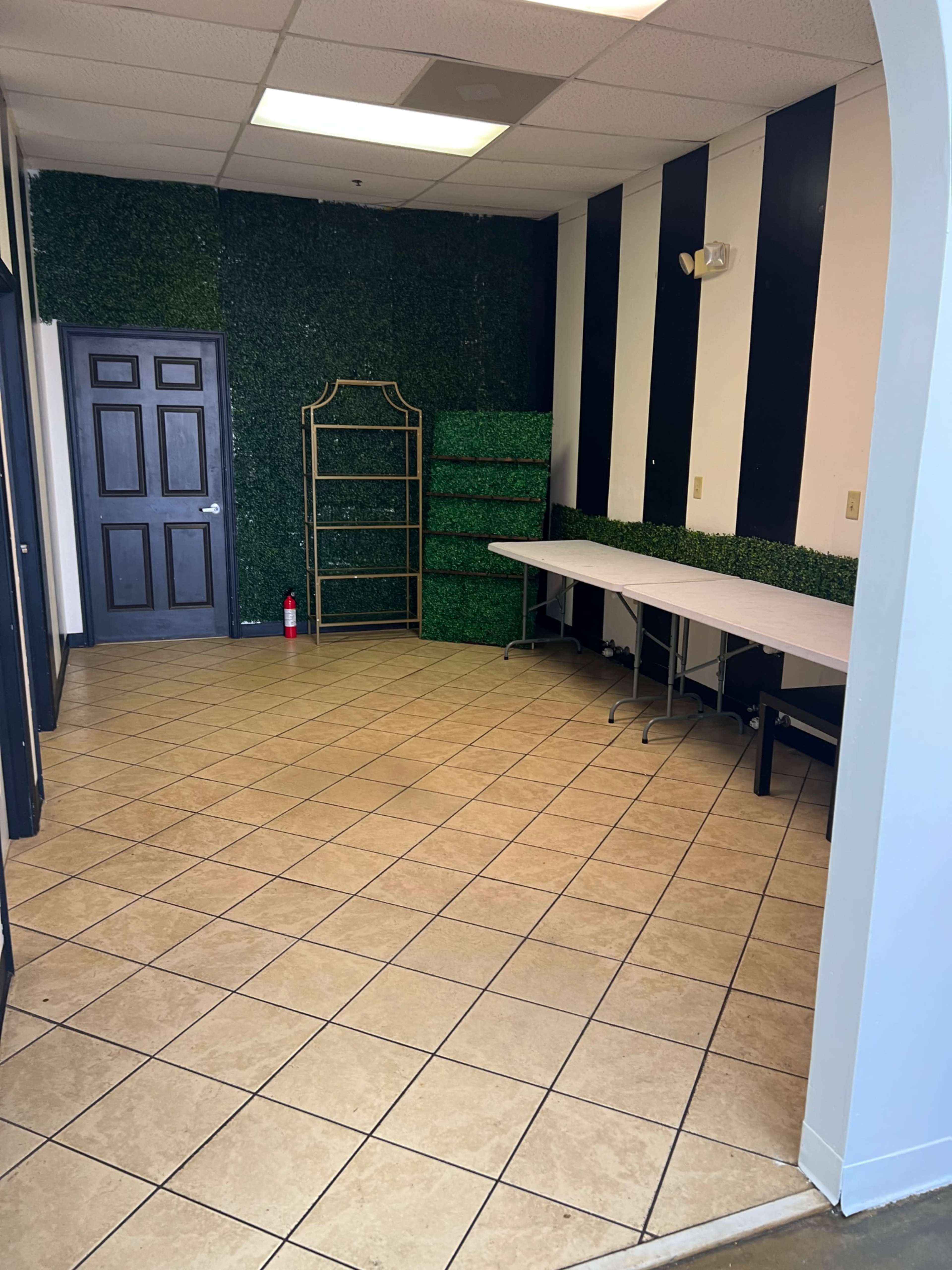 An empty room with green grass-like wall decor, black and white striped walls, a folding table, and a shelving unit.