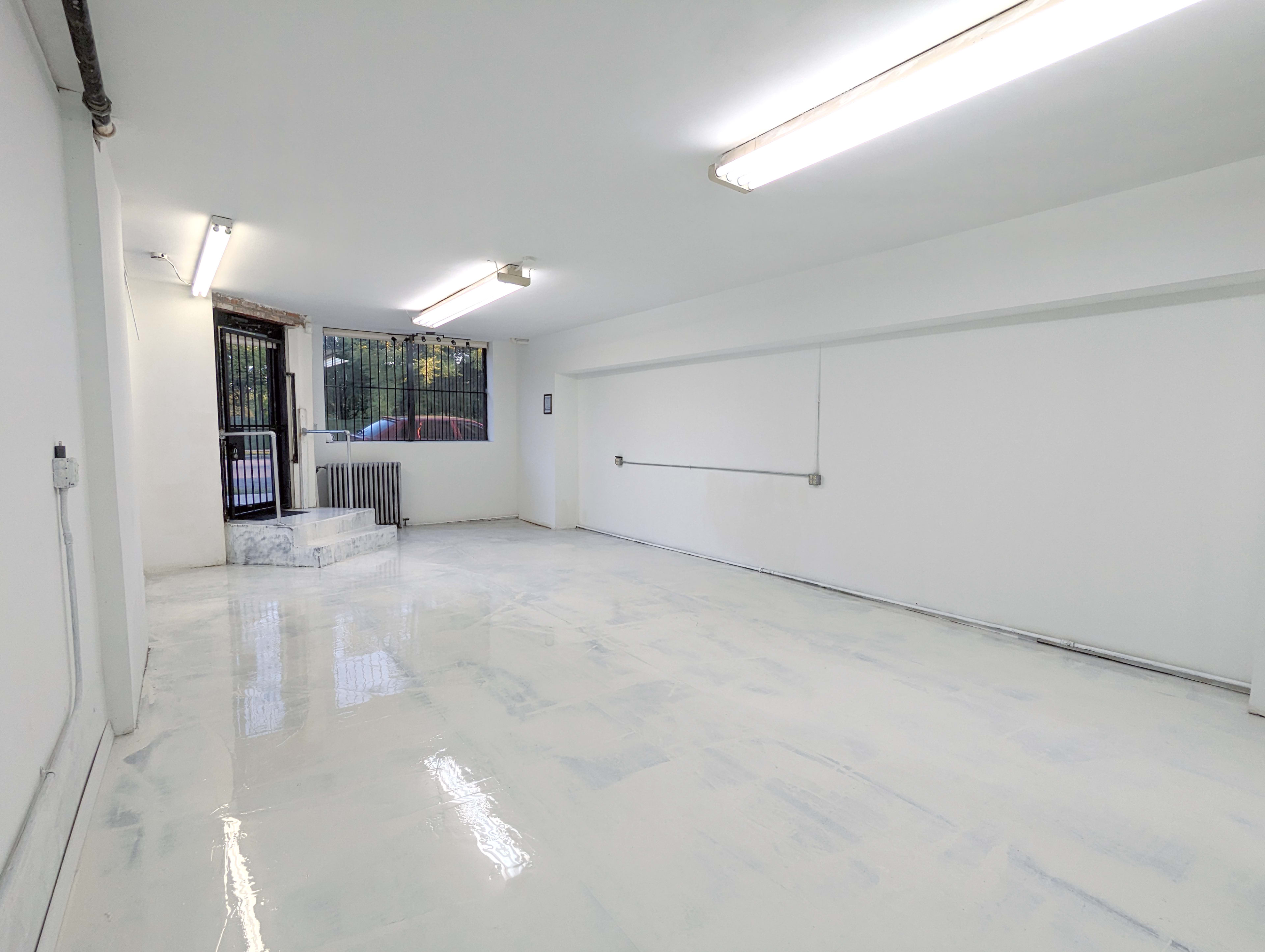 An empty, white-walled room with a glossy floor and a window leading to an outdoor area.