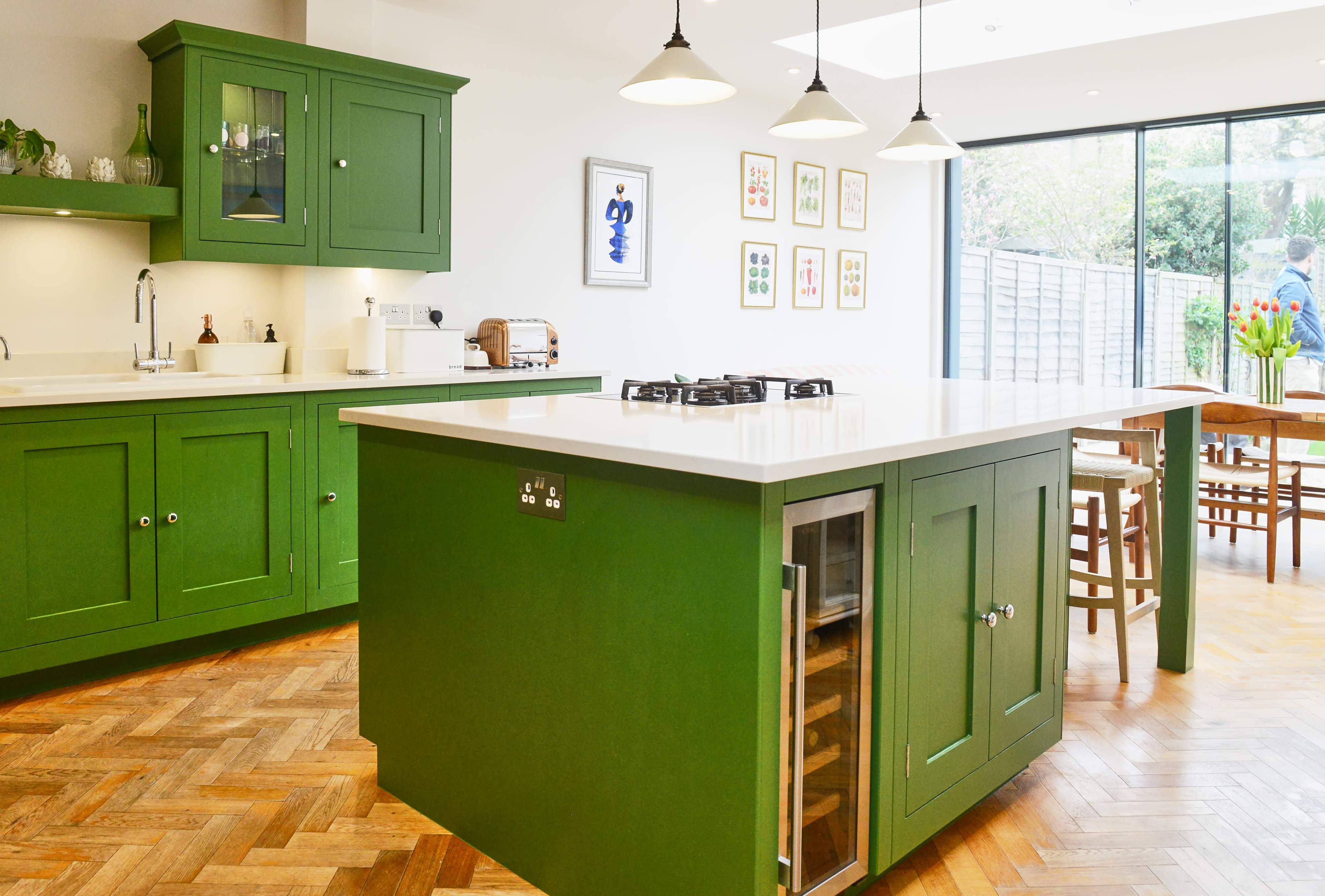 A modern kitchen with green cabinetry and a central island featuring a gas cooktop and a built-in wine cooler.