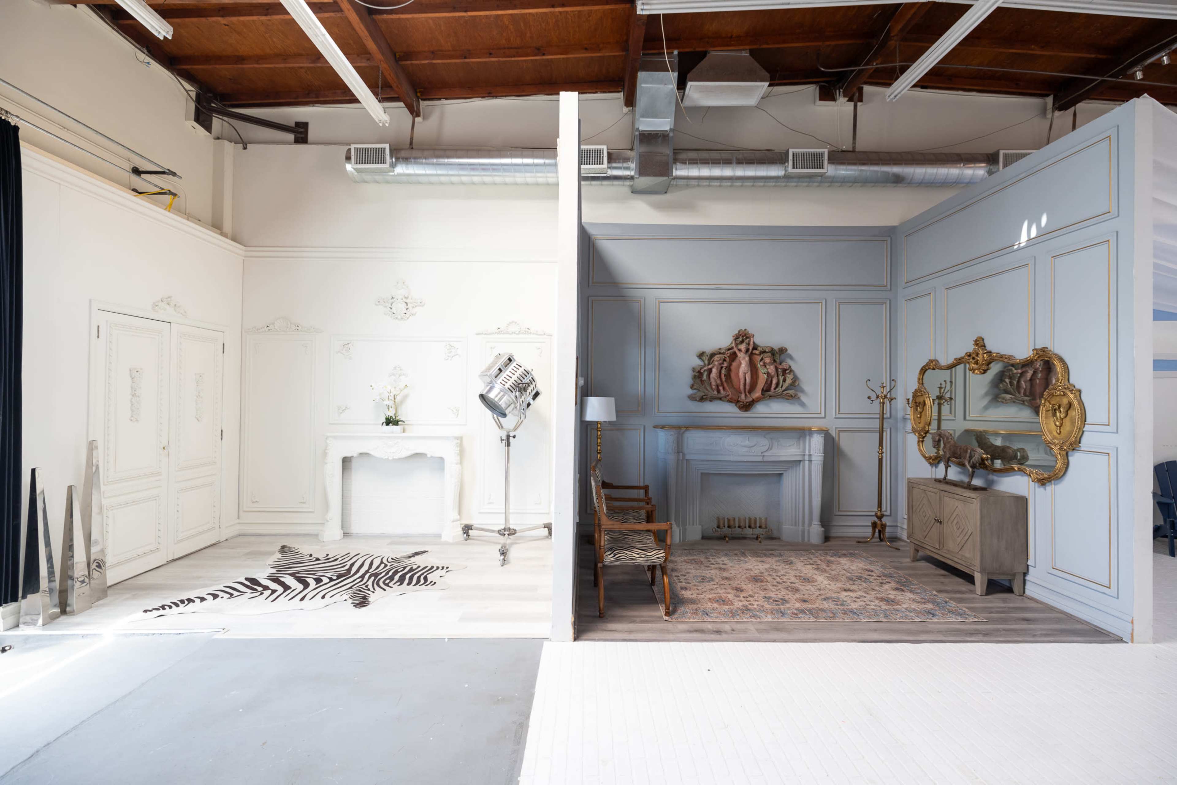 The image shows a split interior space featuring two distinctly styled rooms, one with ornate white decor and the other with a blue-toned design and vintage furnishings.