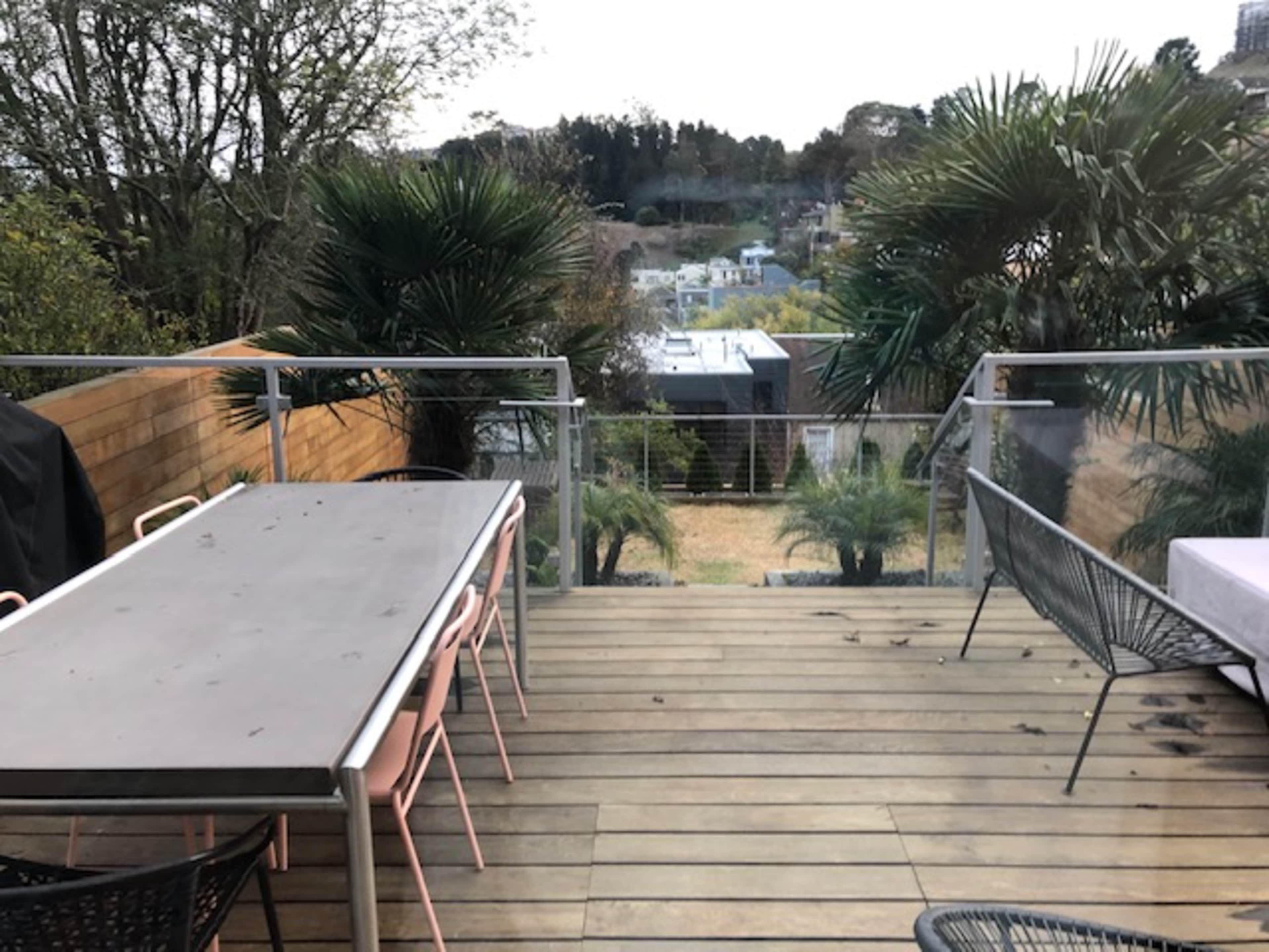 A wooden deck with a table and chairs overlooking a garden and houses in the distance.