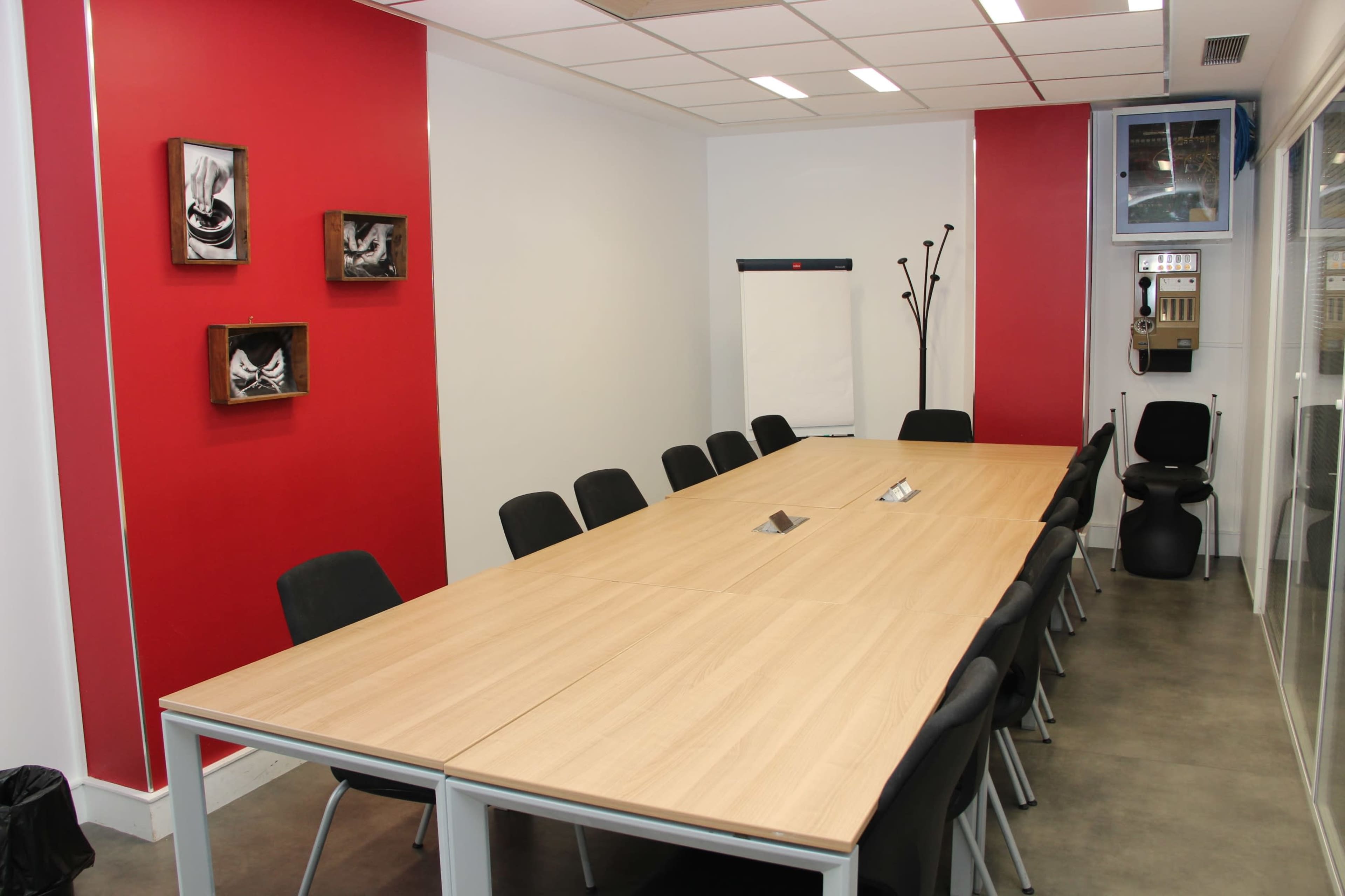 A modern conference room with a long wooden table surrounded by black chairs, red accent walls, and a whiteboard on one side.