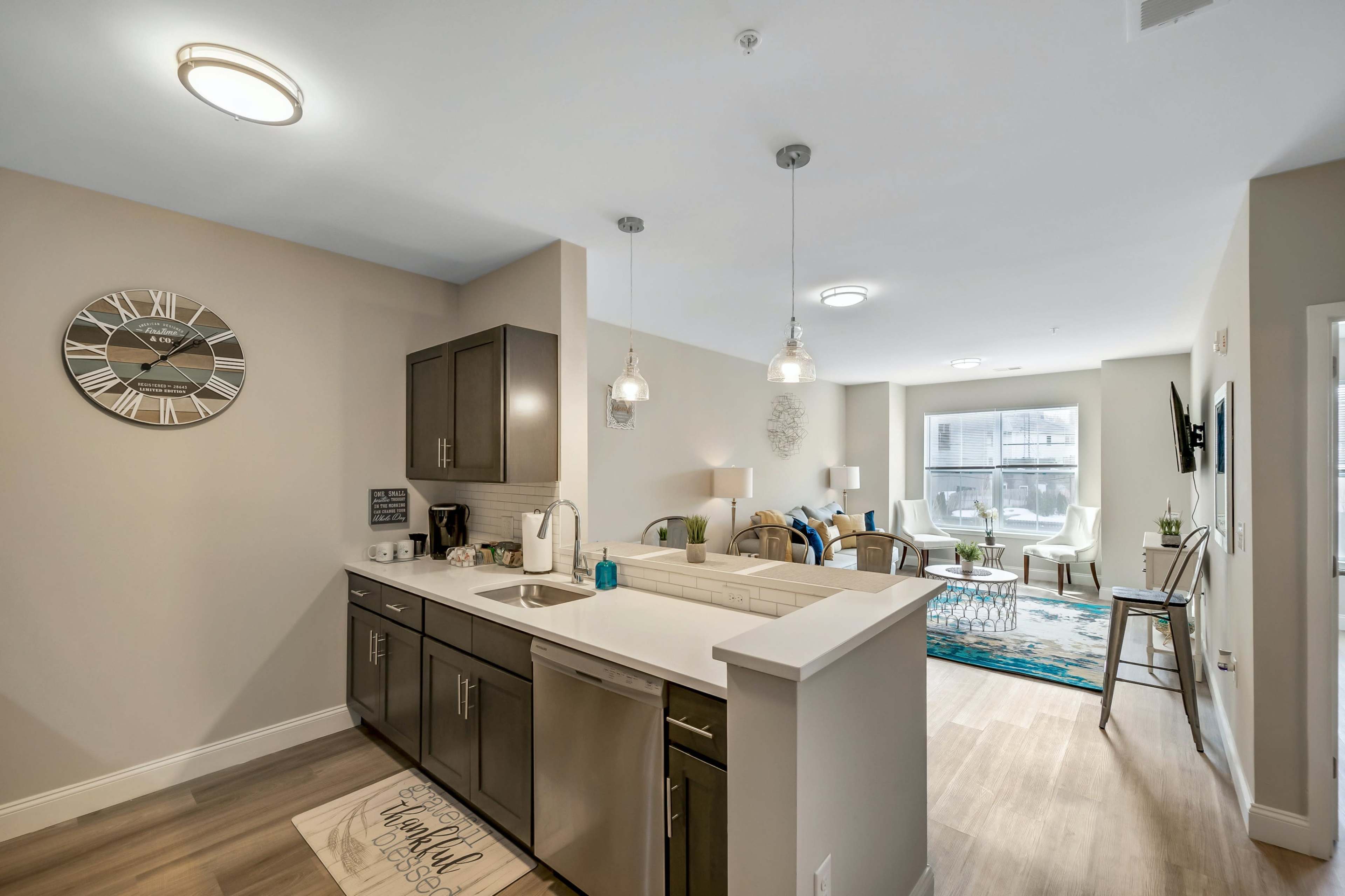 A modern open-concept kitchen and living area with light-colored walls, stainless steel appliances, and a cozy seating arrangement.