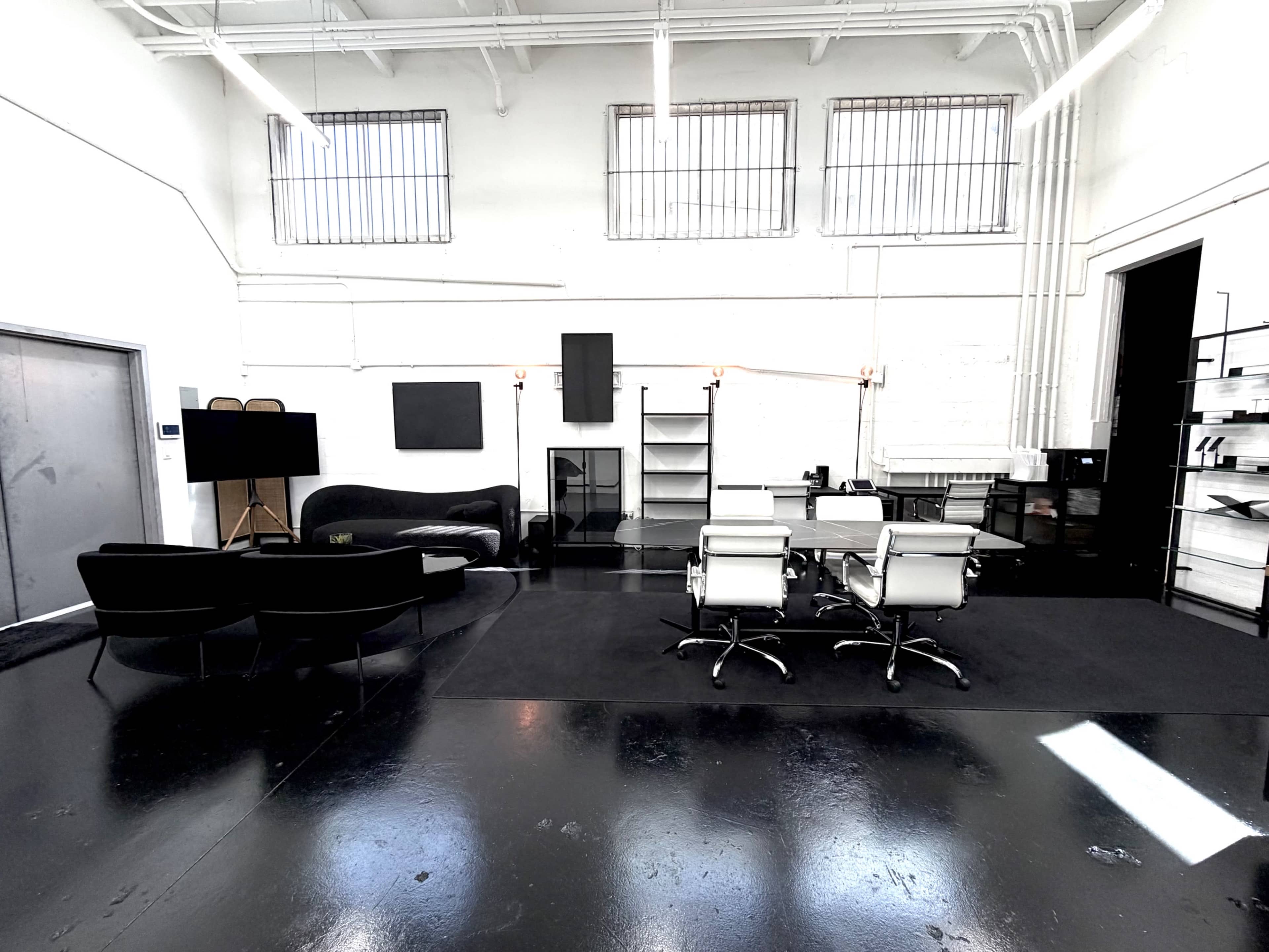 The image shows a modern, spacious office area with black flooring, a couch, several armchairs, and a conference table with ergonomic chairs.