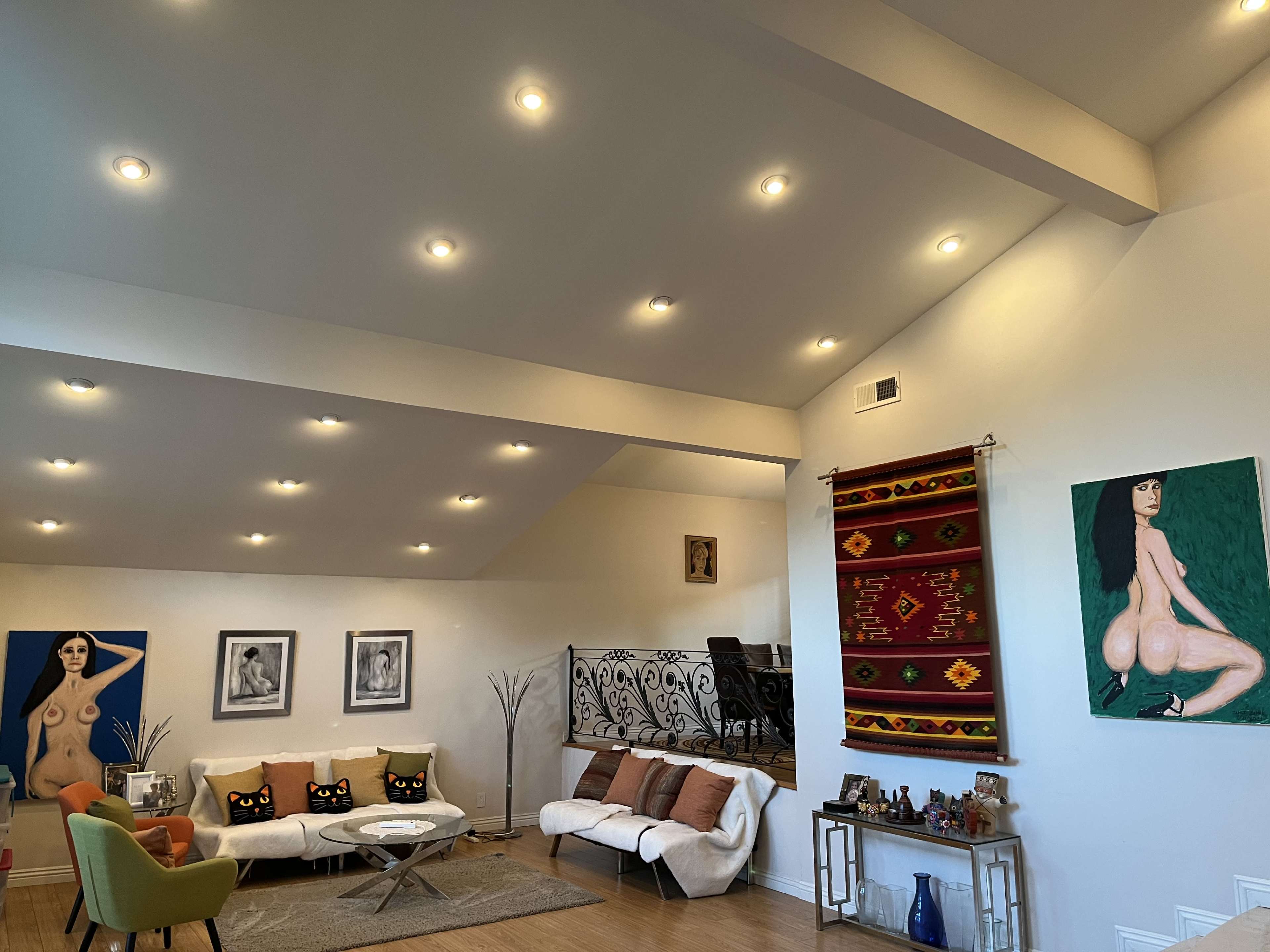 The living room features a white sectional sofa, a round coffee table, and various artworks displayed on the walls, including paintings and photographs.