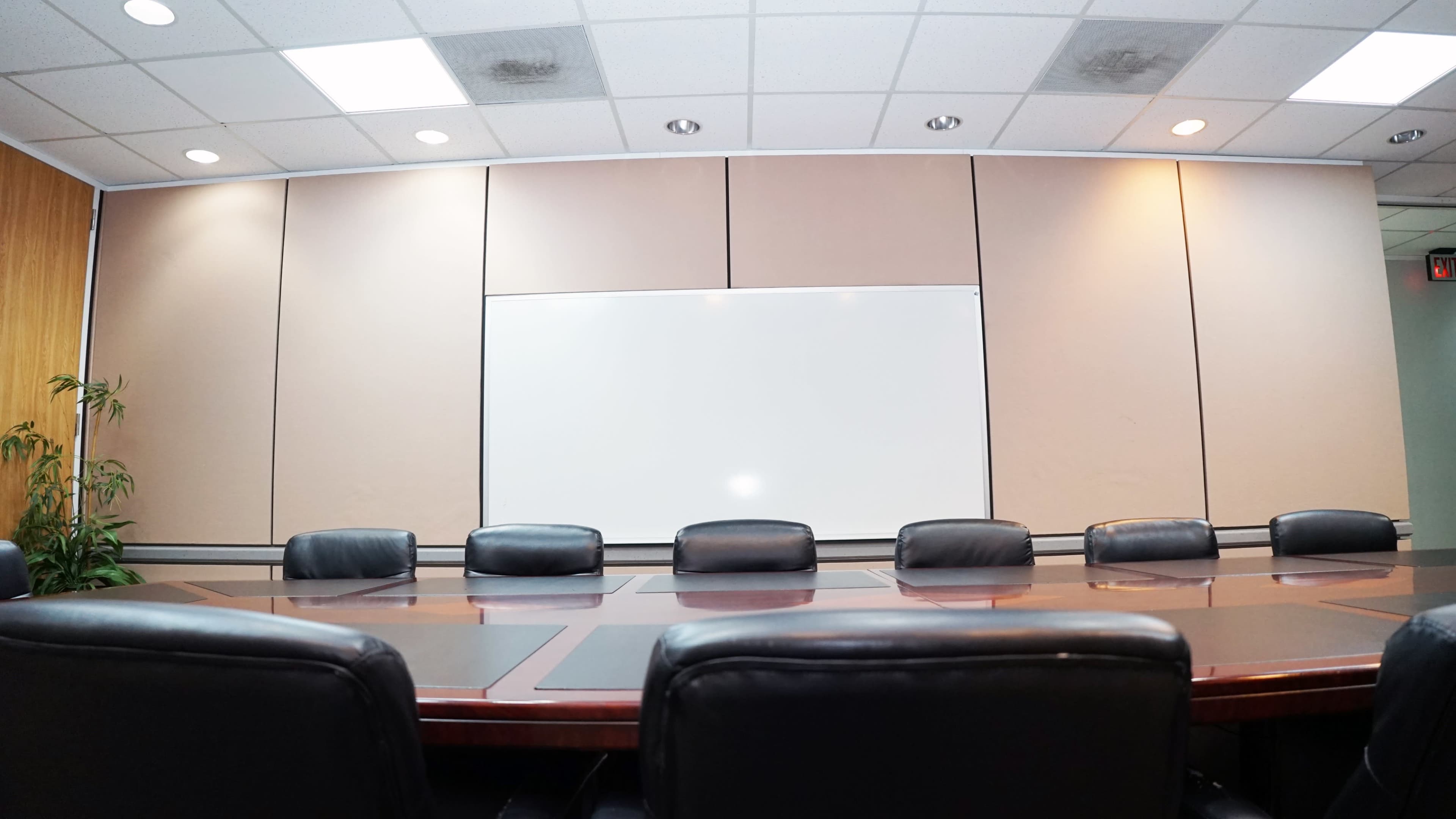 A conference room with a long wooden table surrounded by black leather chairs and a whiteboard on the wall.