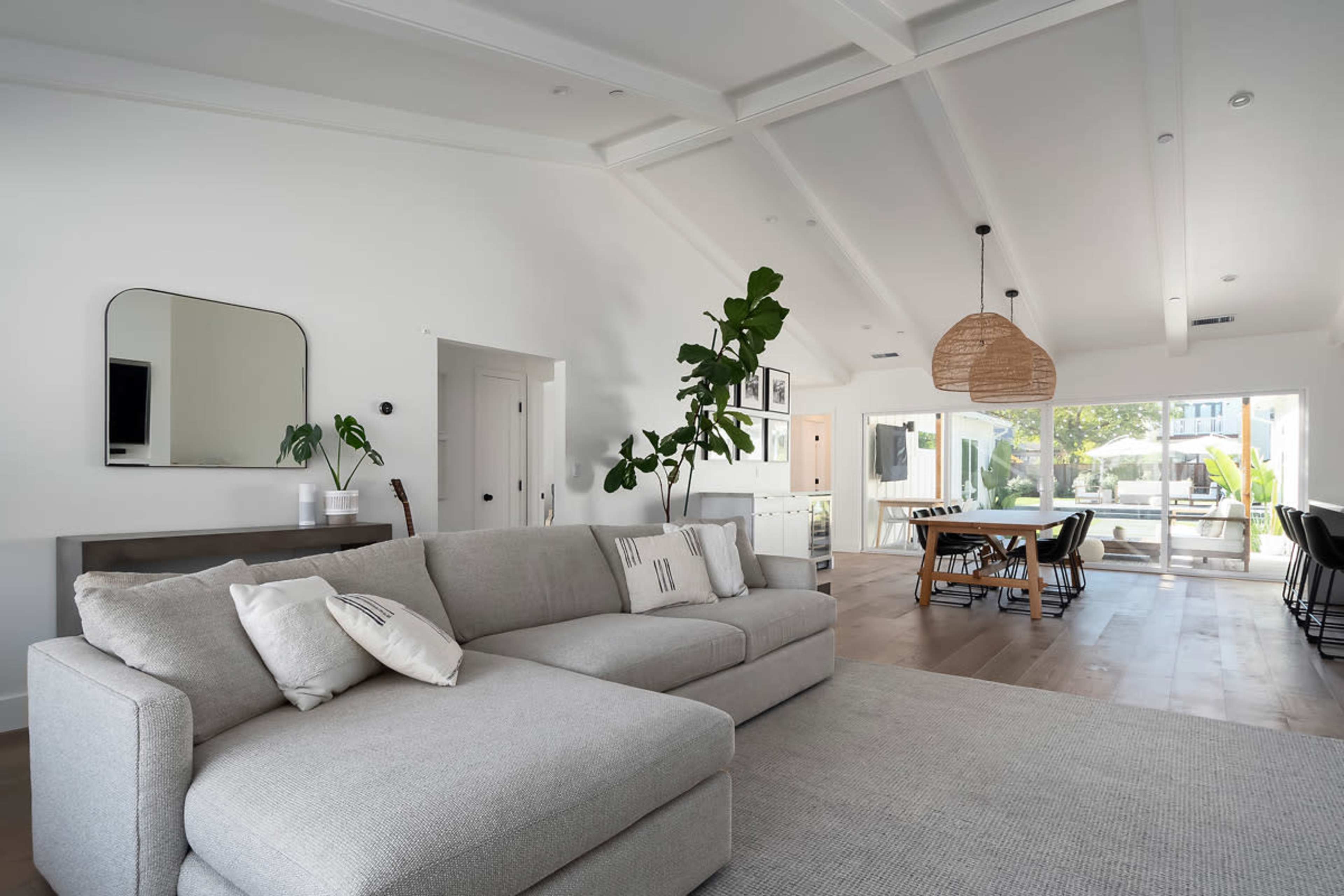 A modern living room with a grey sectional sofa, a large mirror, and a view of an outdoor space through sliding glass doors.