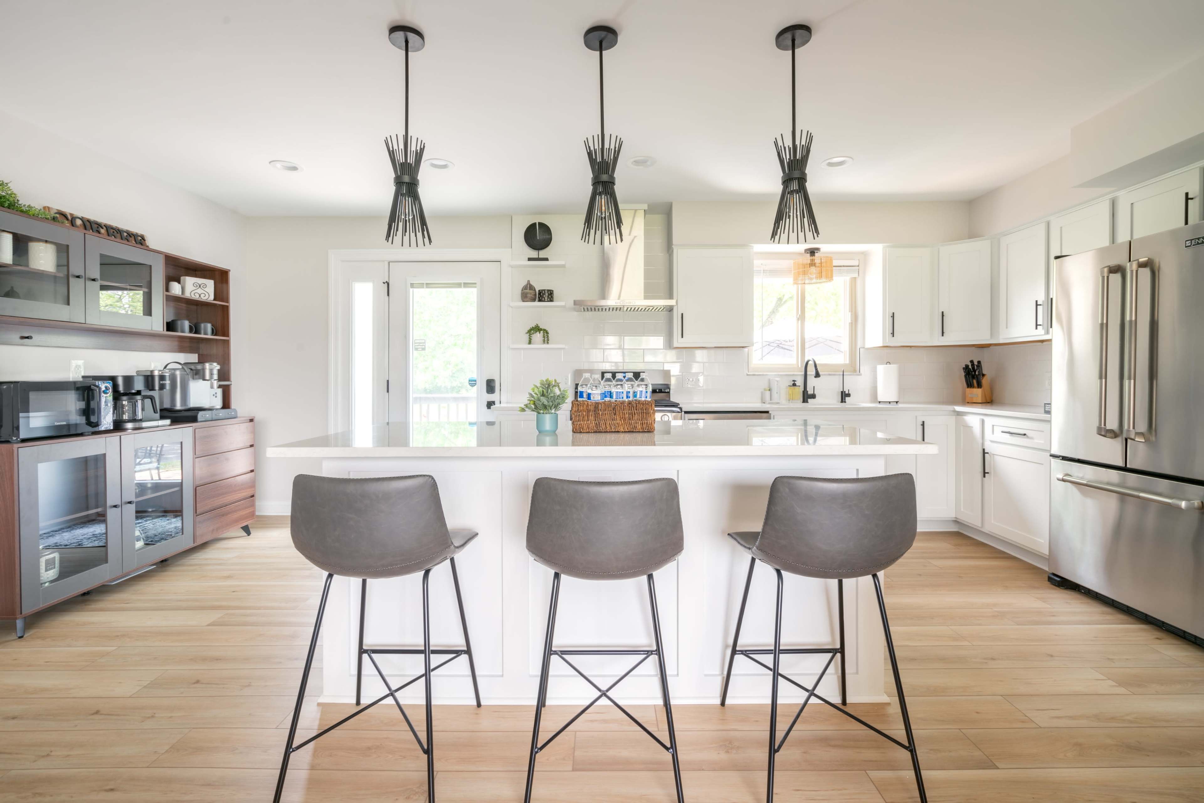 A modern kitchen with white cabinetry, a central island with three stools, and stainless steel appliances.
