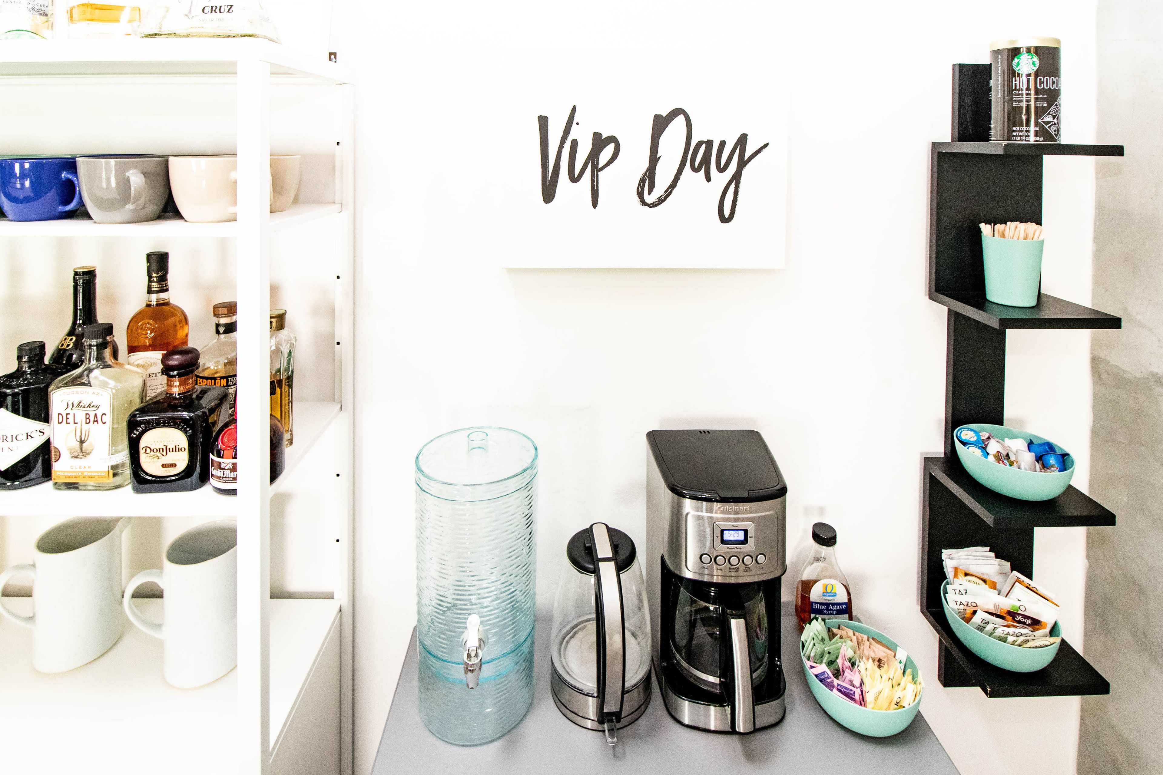 A refreshments area featuring a coffee maker, a water dispenser, assorted snacks, and beverage options on shelves labeled "VIP Day."
