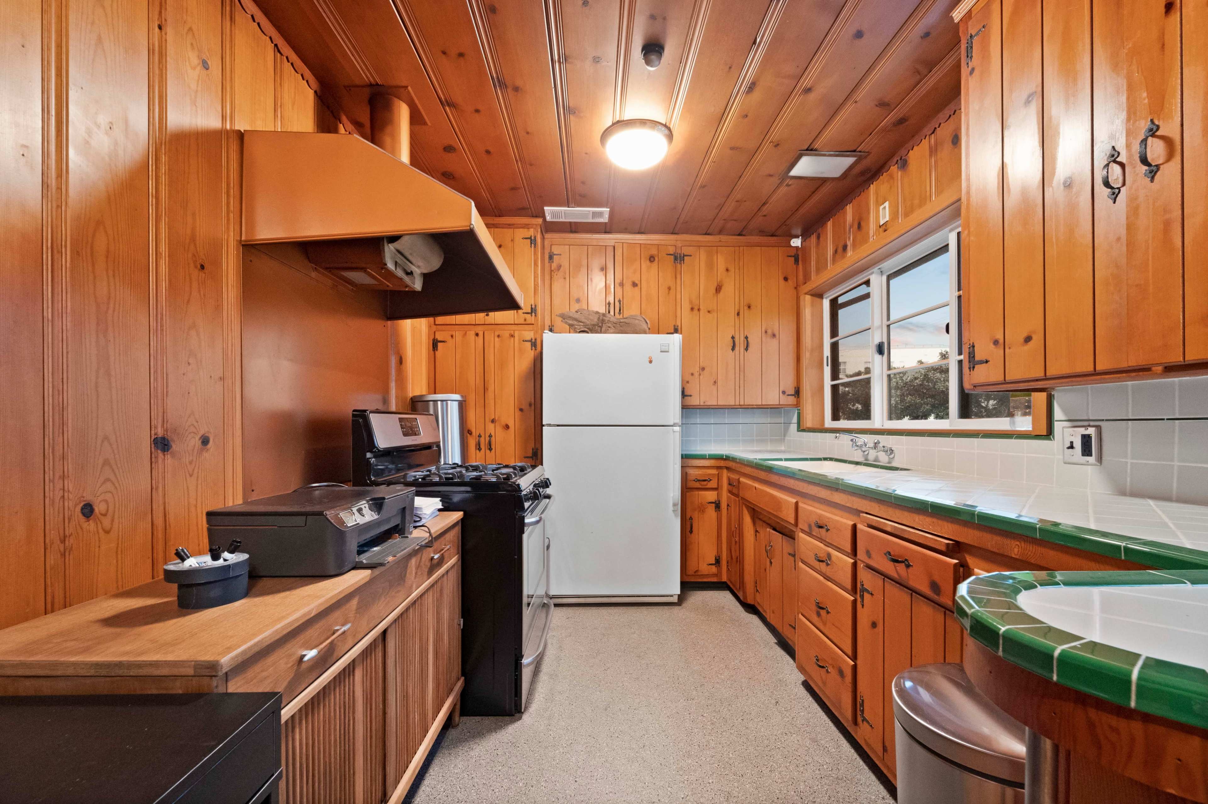 A wooden kitchen features a white refrigerator, a gas stove, and ample cabinetry along with a green counter.
