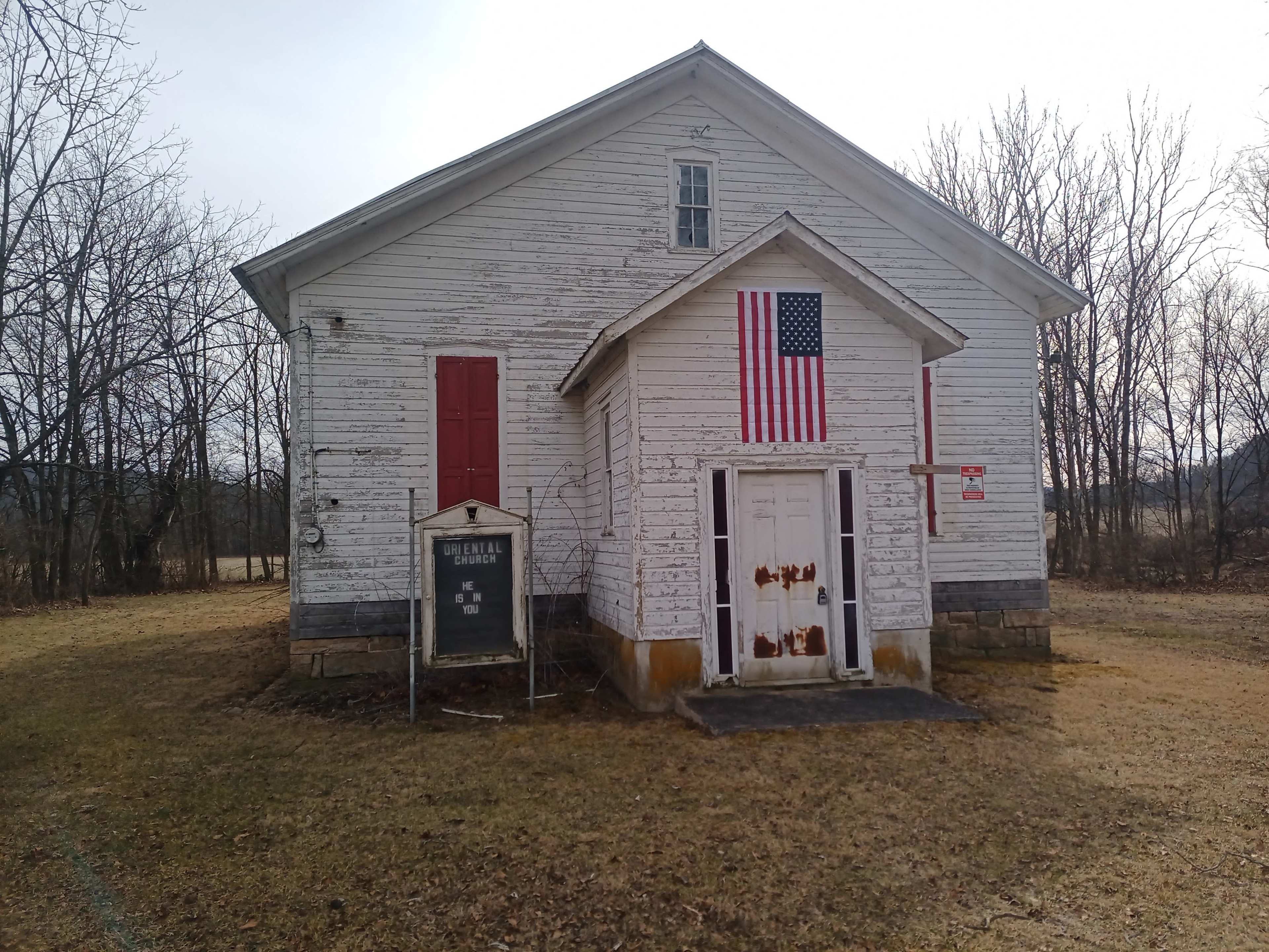A weathered white building with an American flag displayed on the front, flanked by two red doors.