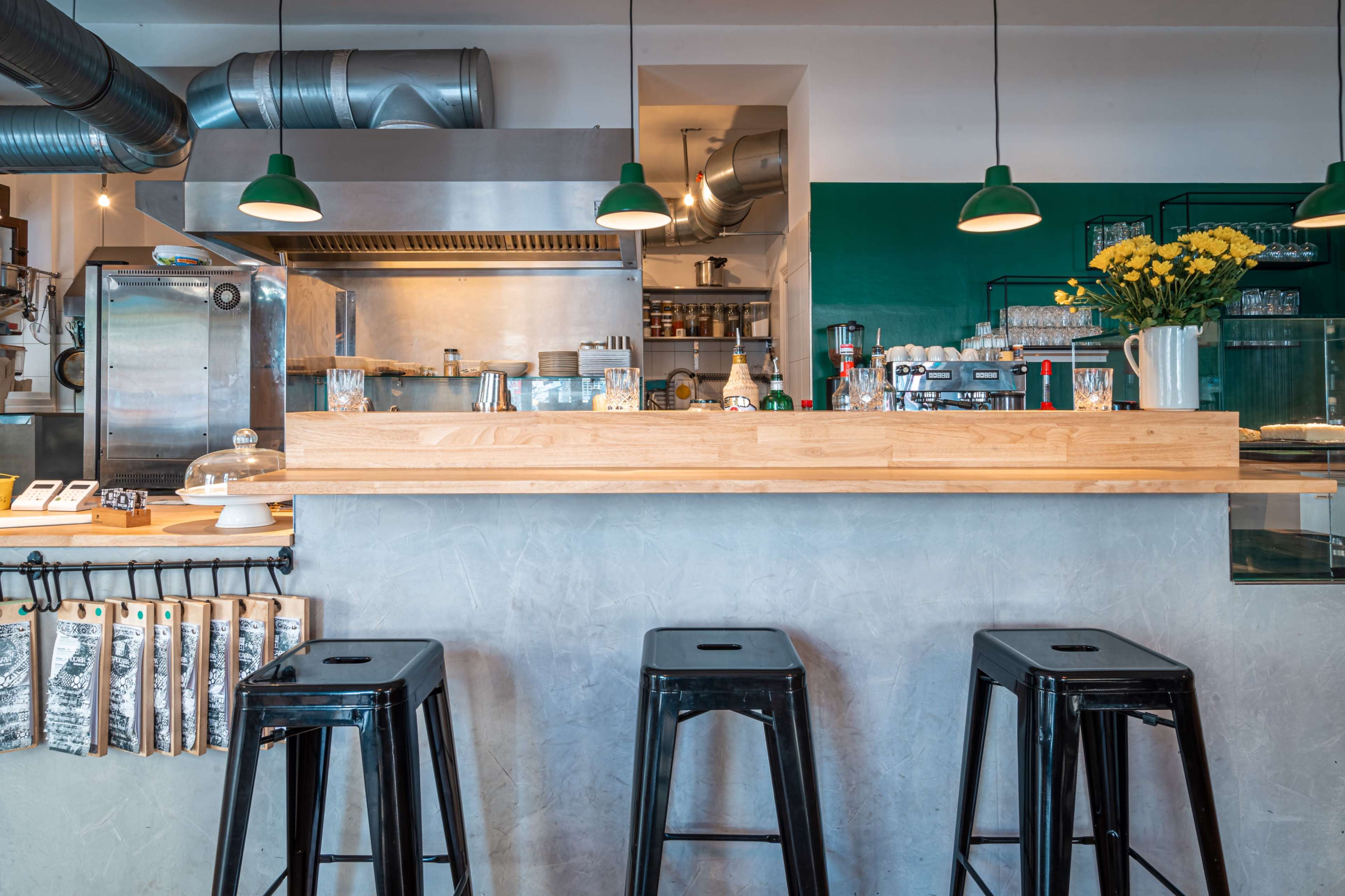 A modern cafe interior with a wooden bar, industrial-style stools, and a green wall behind the counter.