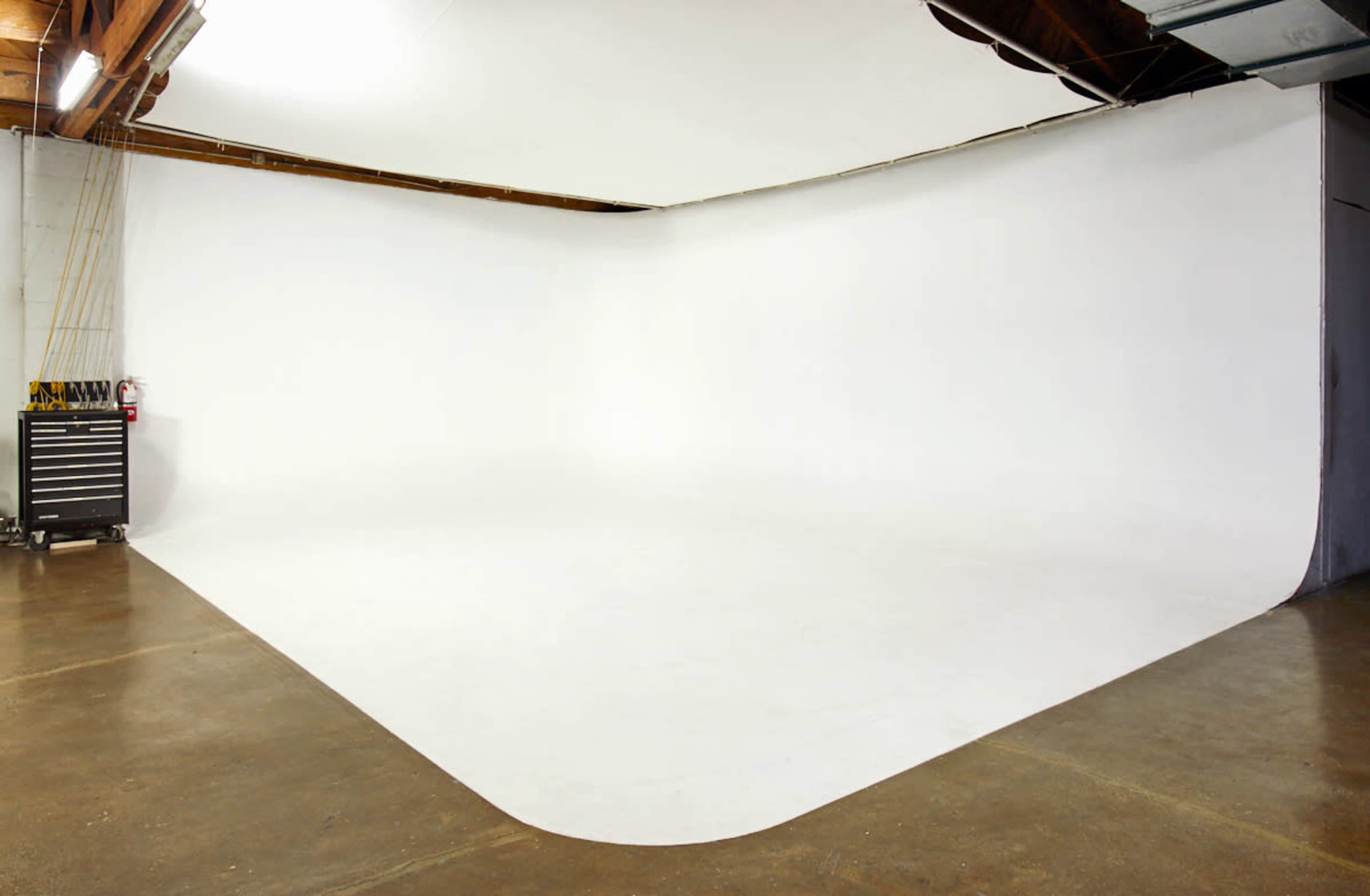 An empty photography studio with a seamless white backdrop and a polished concrete floor.