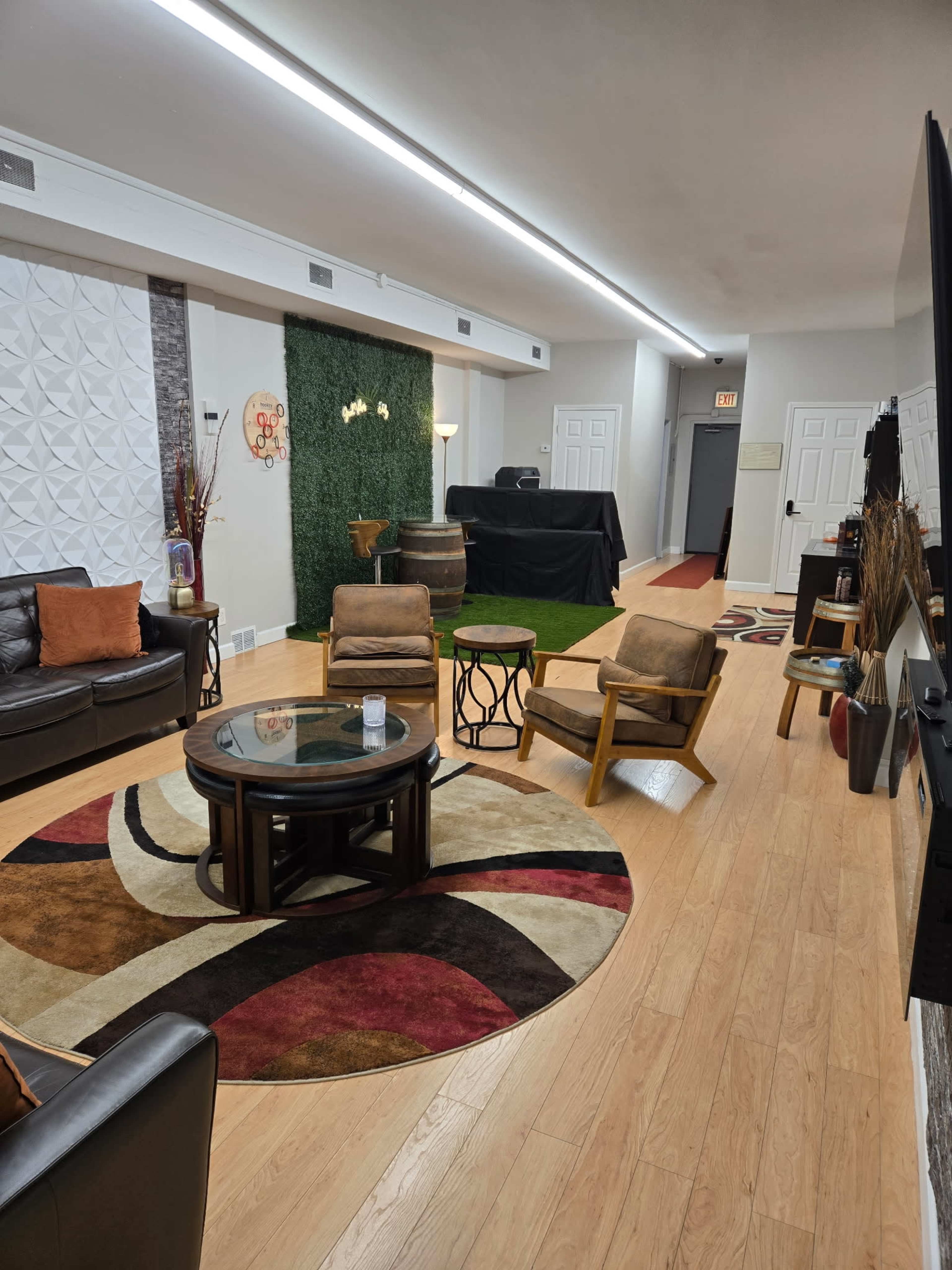 The image shows a modern lounge area with a wooden floor, a circular area rug, several seating options, and a small table in the center.