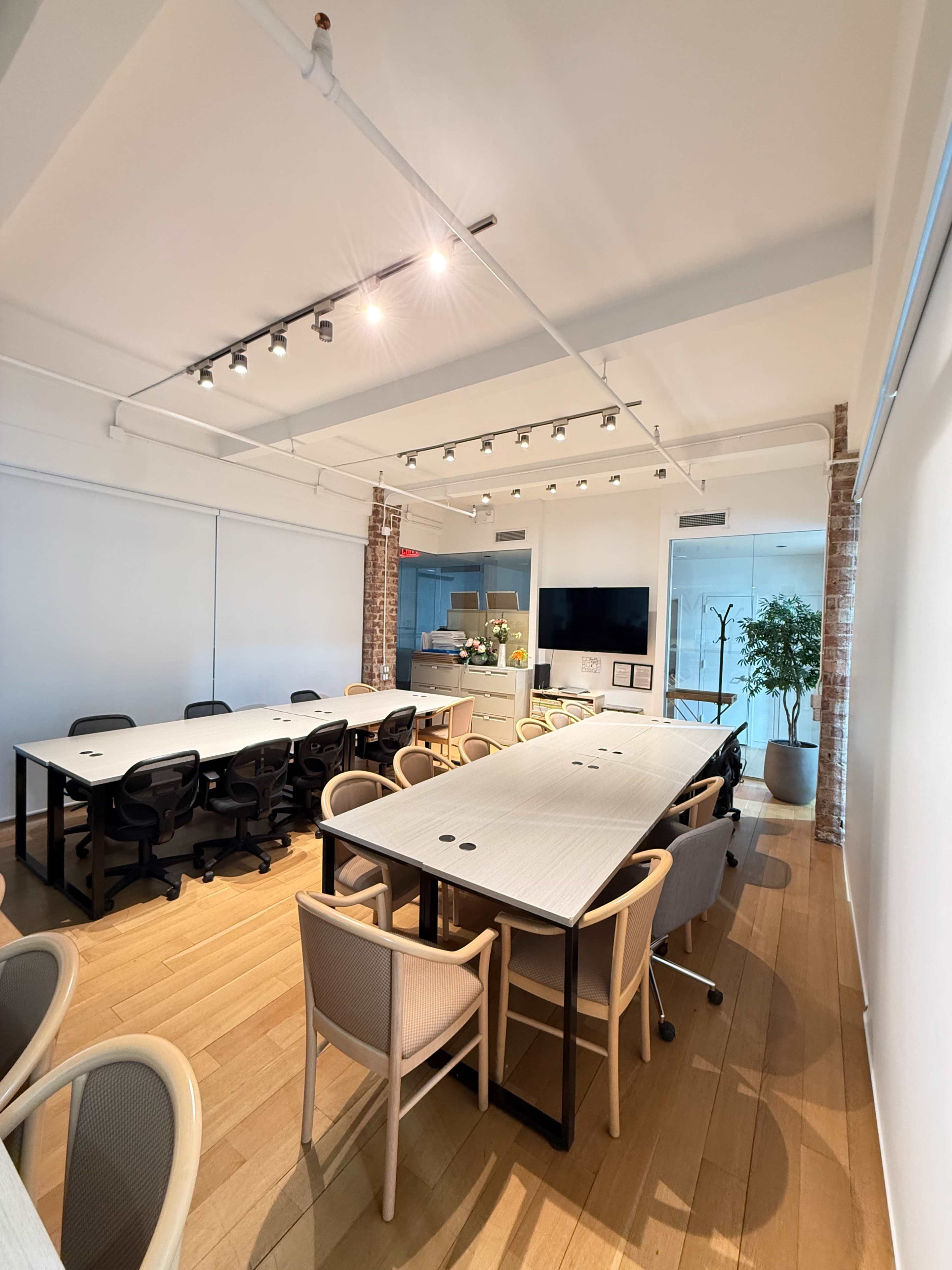 The image shows a modern conference room with a long table surrounded by chairs, a large screen on the wall, and large windows allowing natural light.