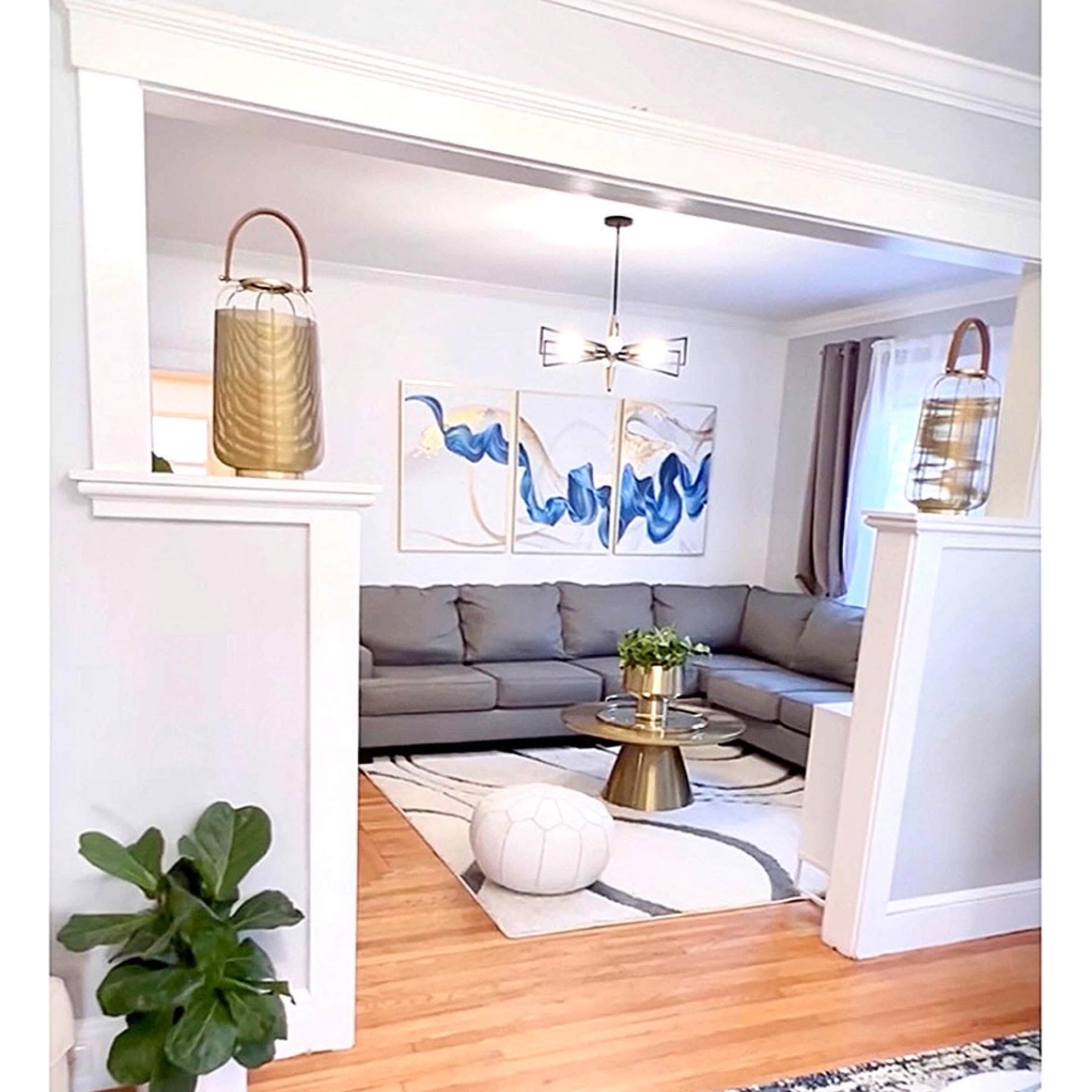 A living room with a gray sectional sofa, a coffee table, and two decorative wall art pieces featuring blue and gold colors, framed by two white pillars.