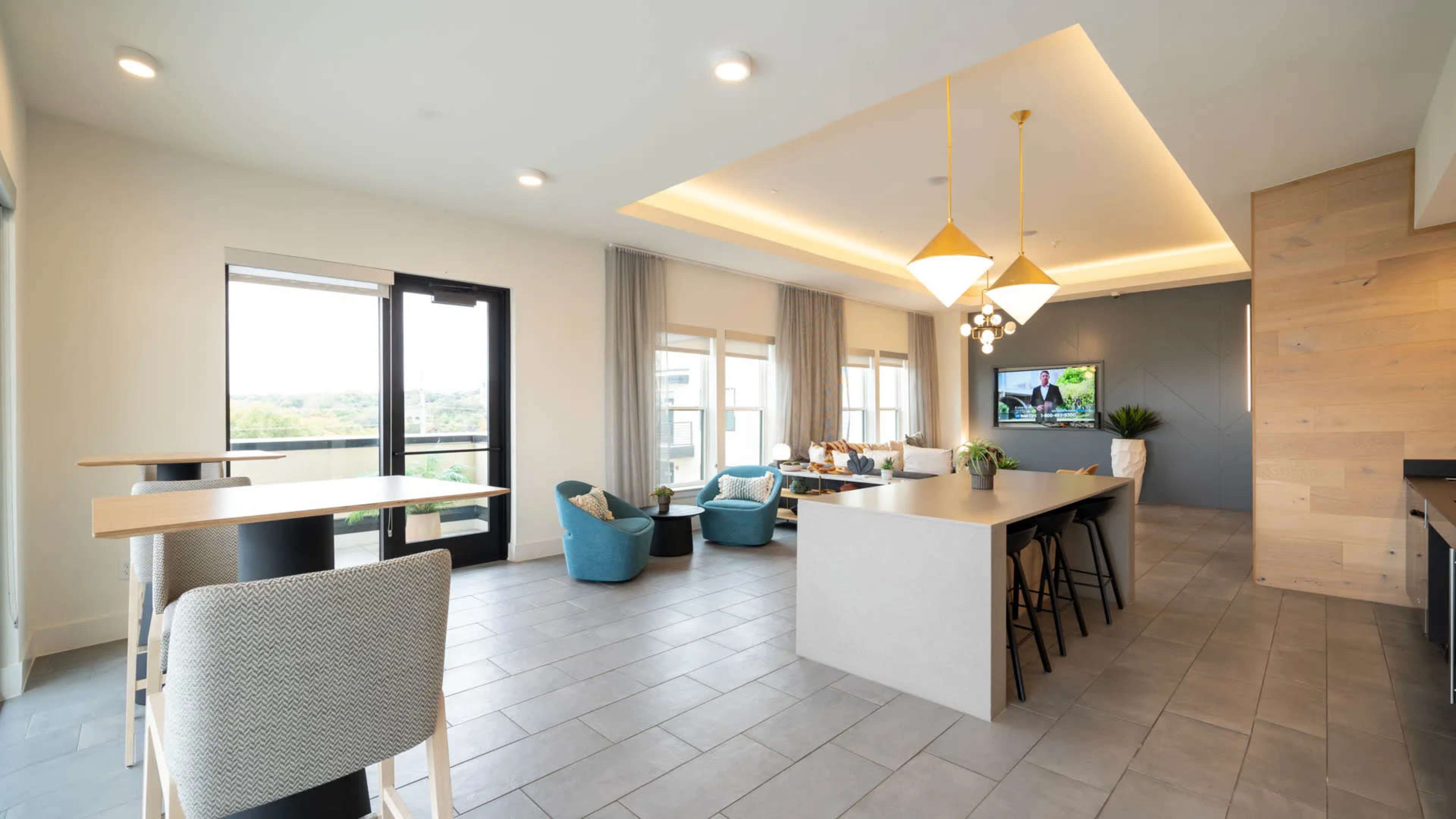 The image shows a modern open-concept living space featuring a kitchen island, seating area, and large windows with views of the outdoors.