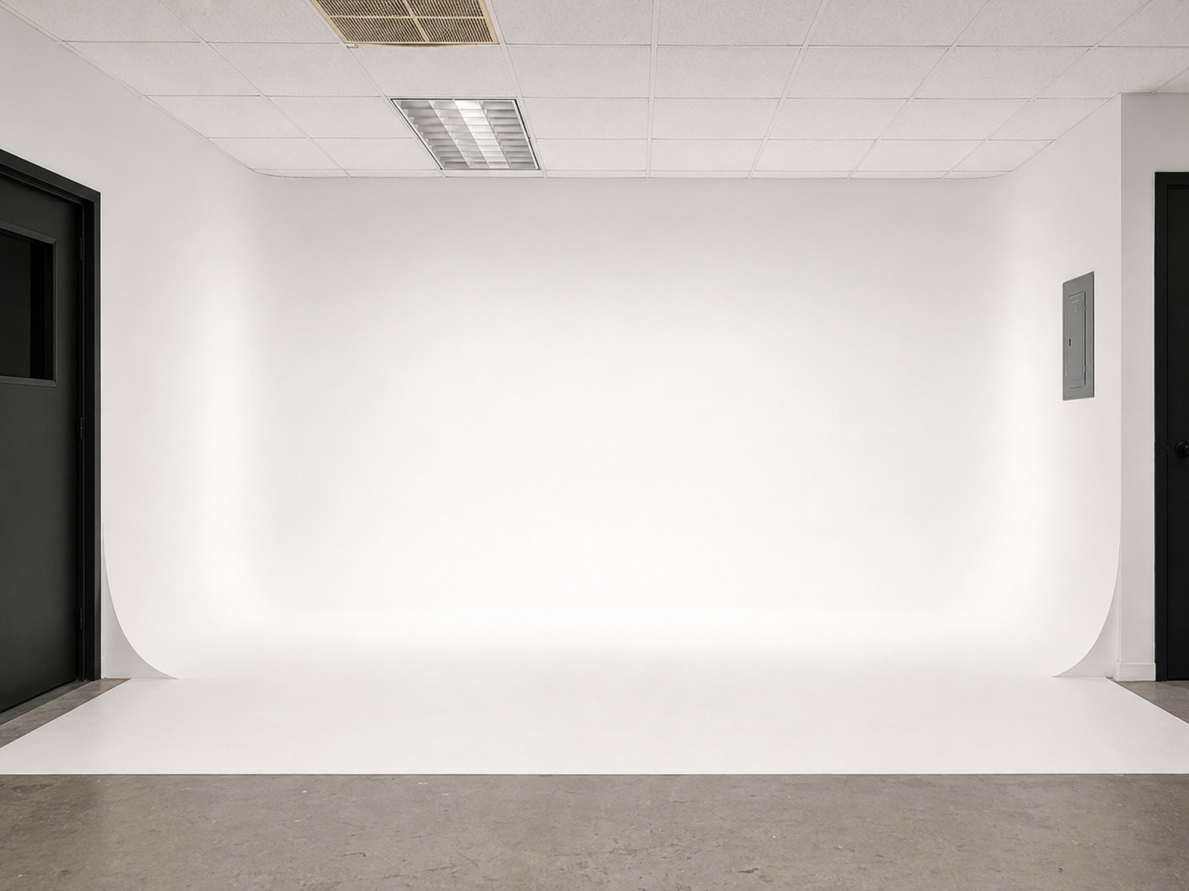 The image shows a simple, empty studio space with a white backdrop and gray flooring.