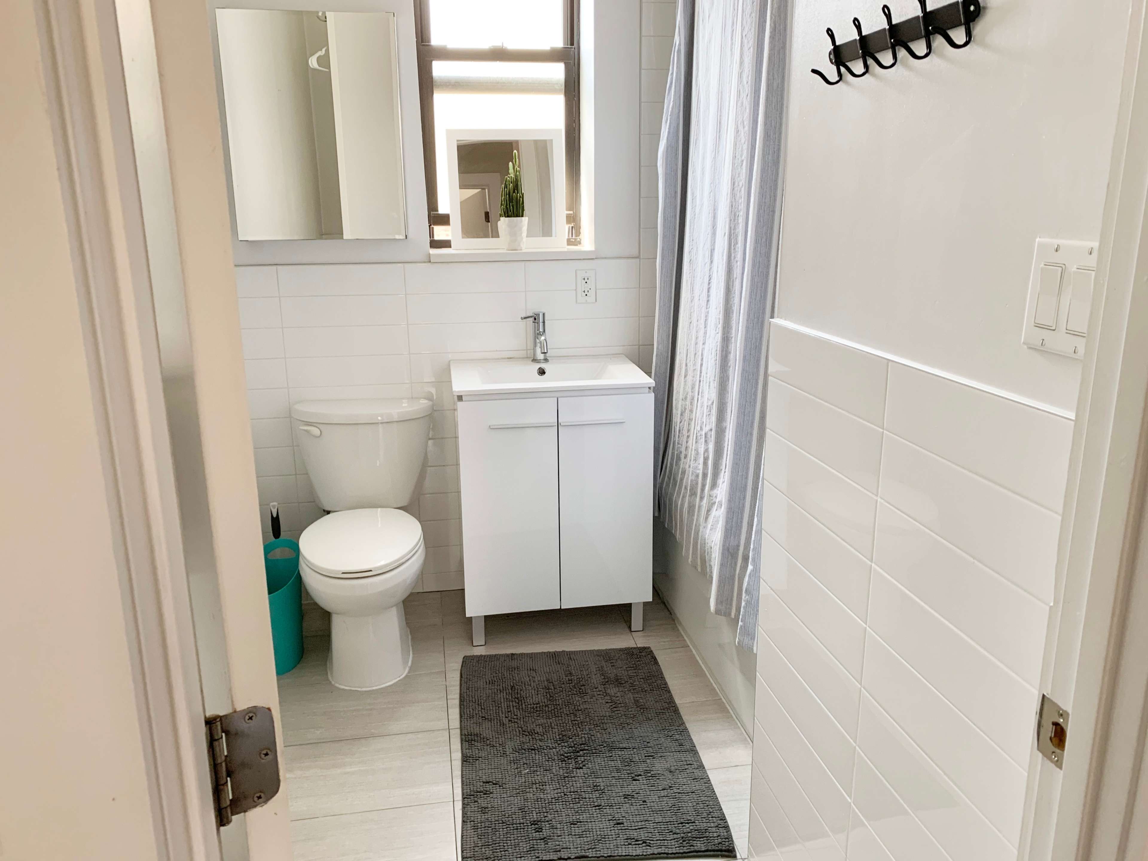 A small bathroom features a white toilet, a sink with a cabinet, a mirror, and a shower with a gray curtain.