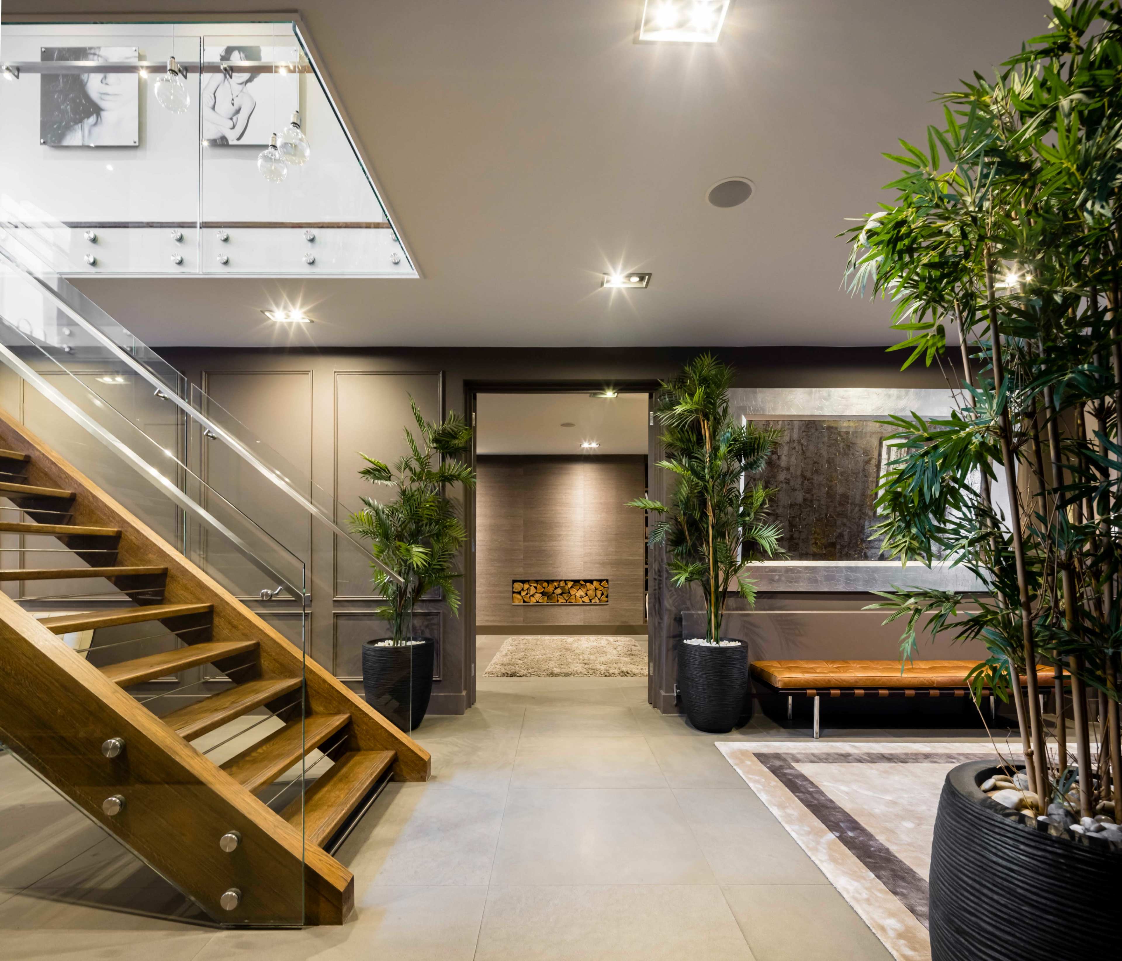 The image shows a modern entryway featuring a wooden staircase, potted plants, and contemporary artwork on the walls.