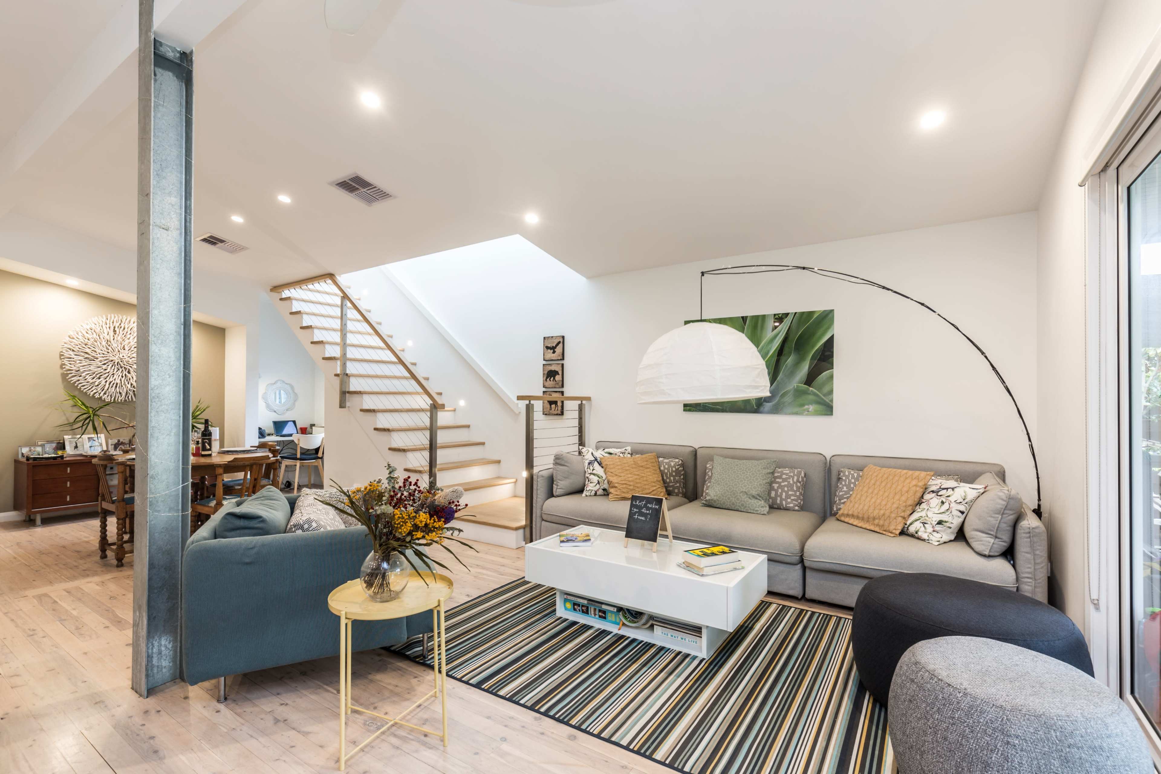 A modern living room with a gray sectional couch, a round coffee table, a striped rug, and a staircase leading to an upper level.