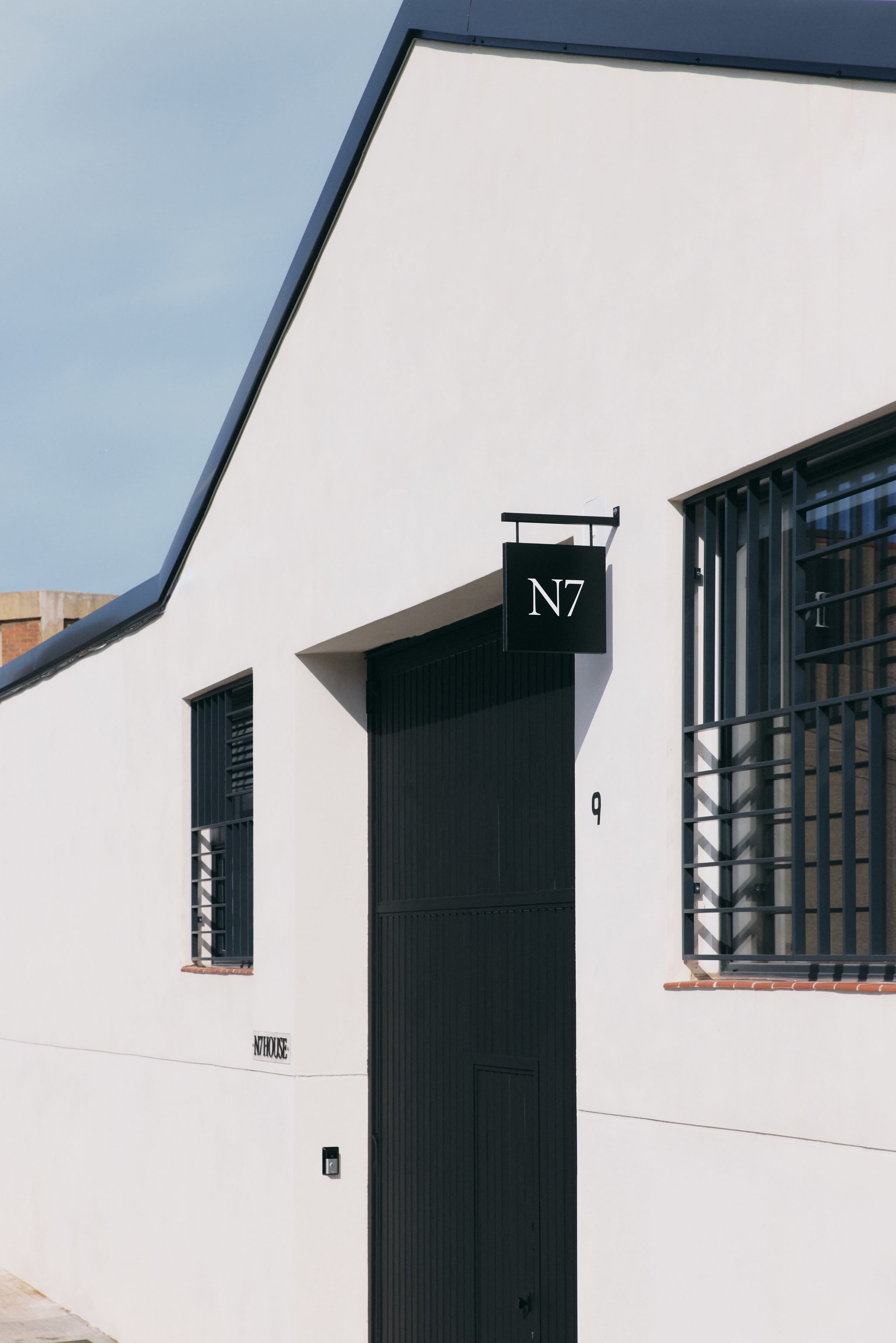 The image shows a modern, minimalist building with a black sign displaying "N7" and large windows with geometric shapes.