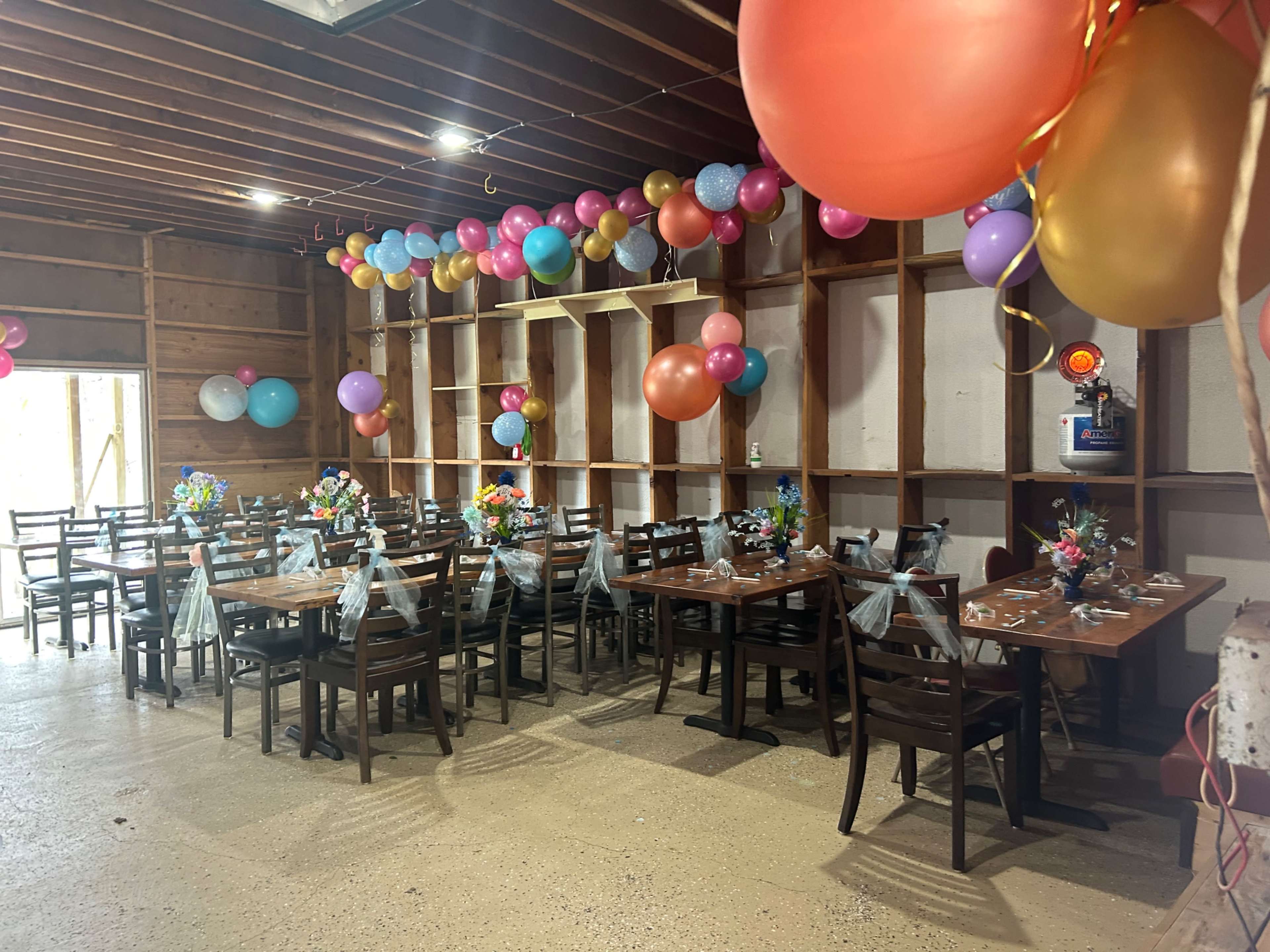 A spacious dining area is decorated with colorful balloons and floral centerpieces on tables set for a celebration.