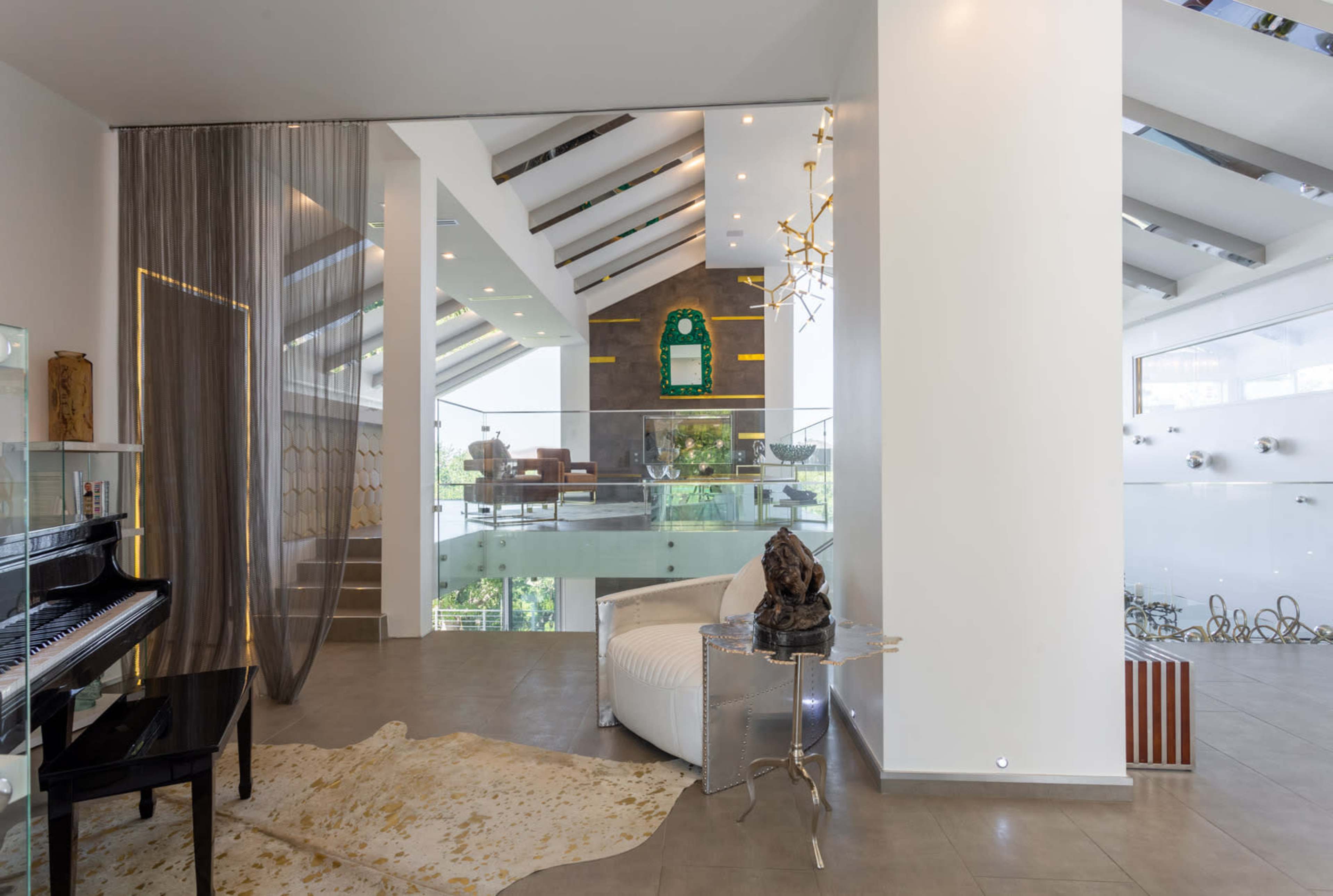 A modern interior space featuring a grand piano, a white armchair, and large windows that allow natural light to illuminate the area.