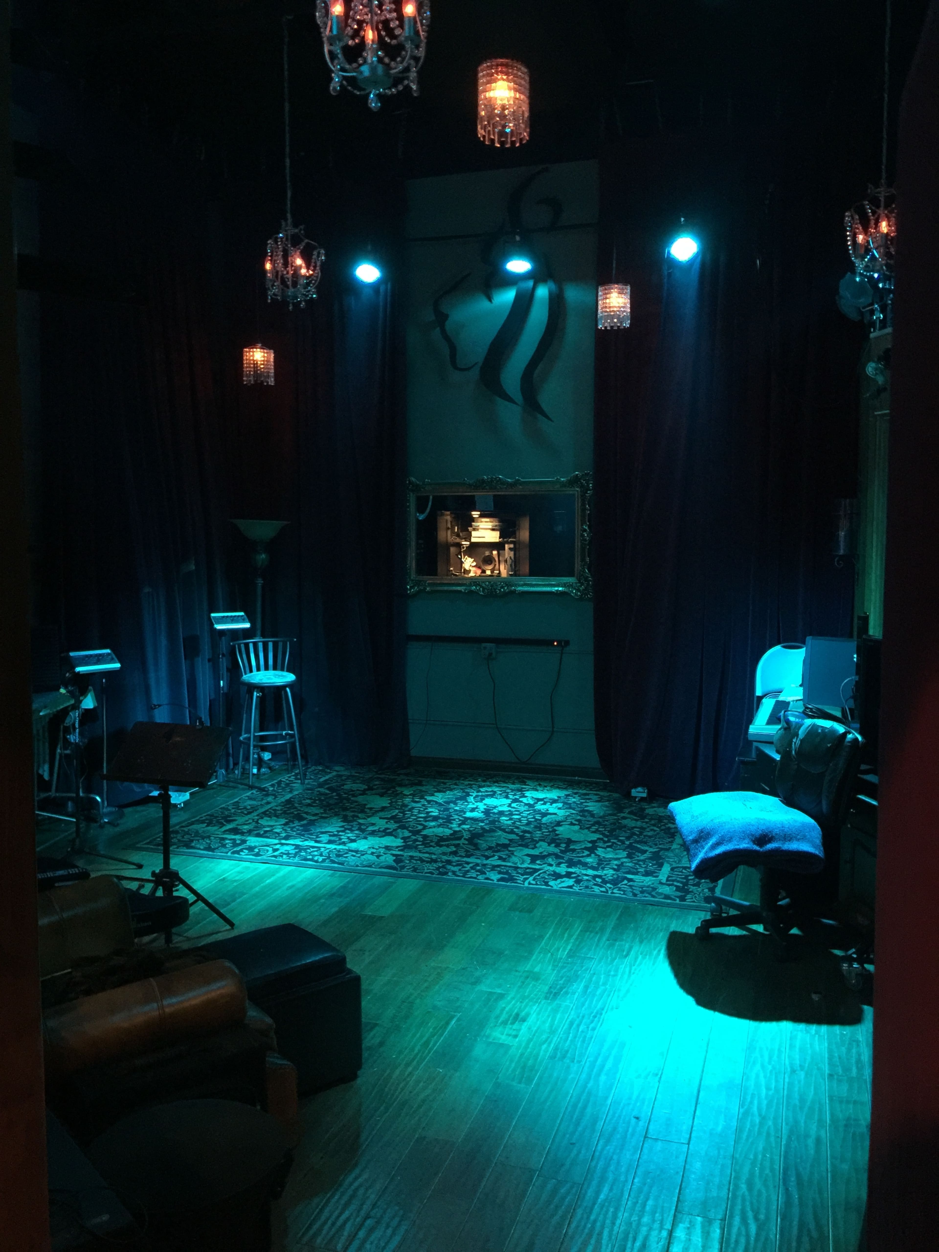 The image shows a dimly lit room featuring elegant chandeliers, blue lighting, and a mix of seating arrangements, including a vintage chair and a couch.