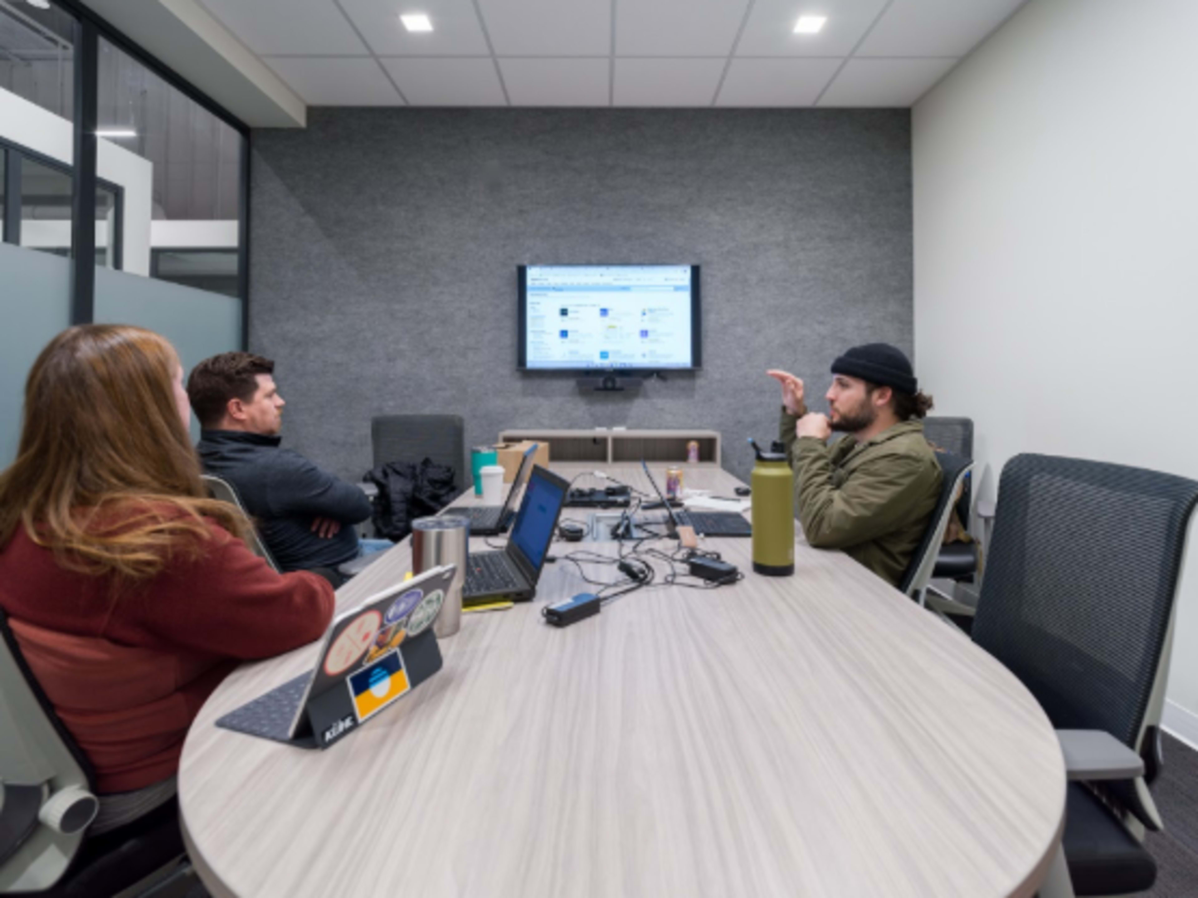 Three people are sitting around a conference table, discussing information displayed on a television screen.
