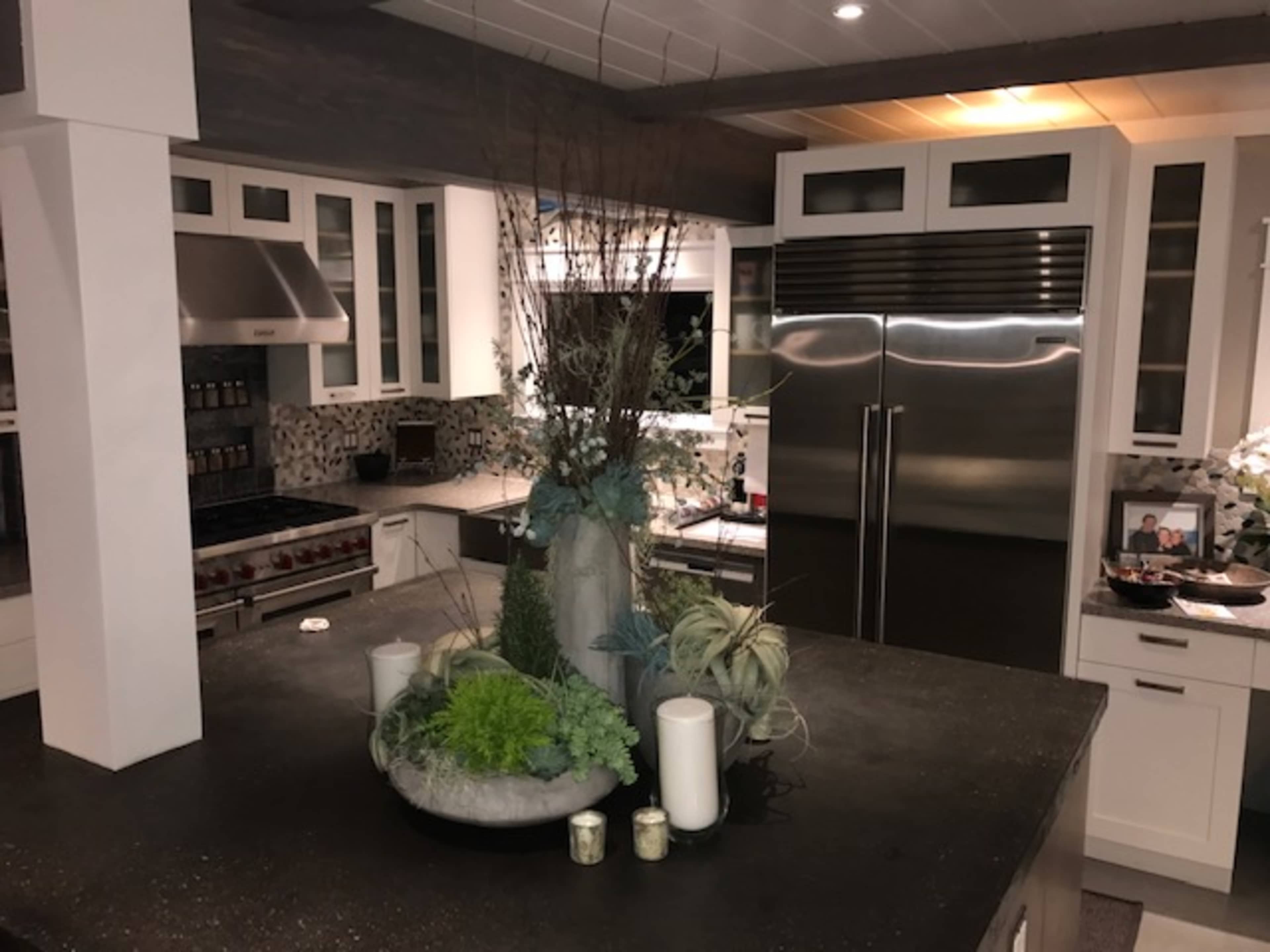 A modern kitchen featuring a large island with a decorative centerpiece, stainless steel appliances, and light cabinetry.