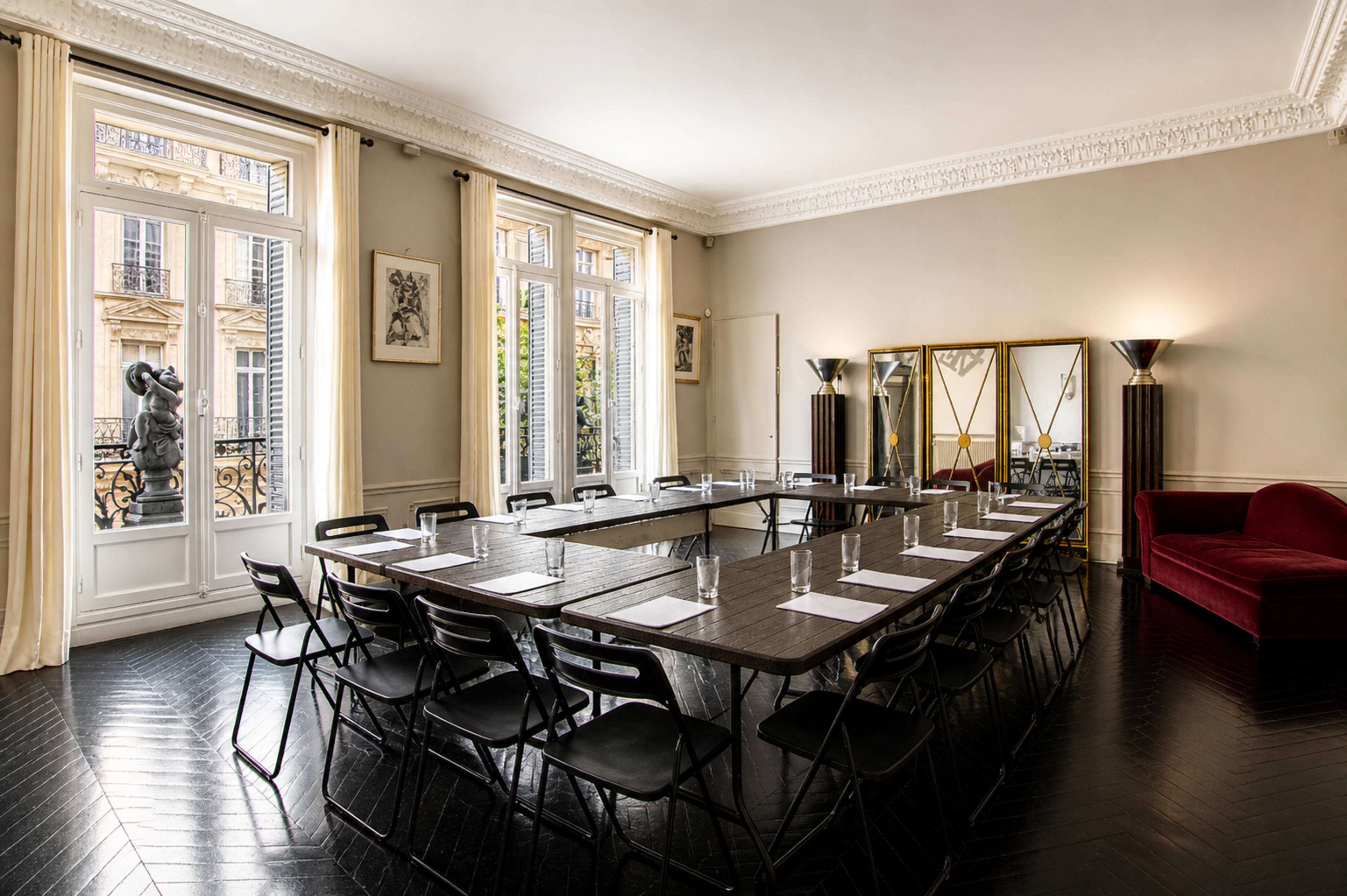 The image shows a spacious conference room with a long rectangular table surrounded by chairs, large windows letting in natural light, and a red couch in one corner.