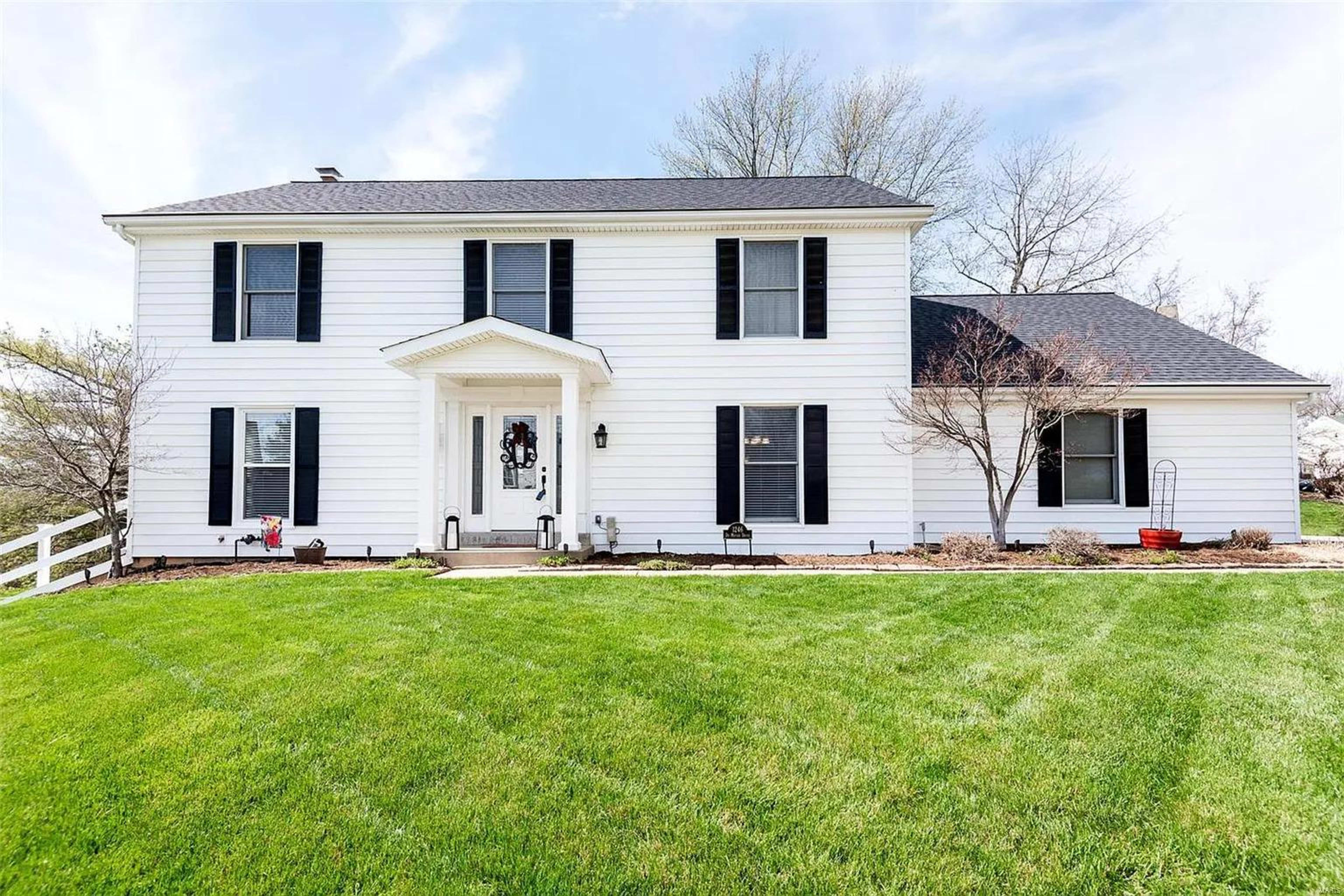 A two-story white house with black shutters and a front porch sits on a green lawn.
