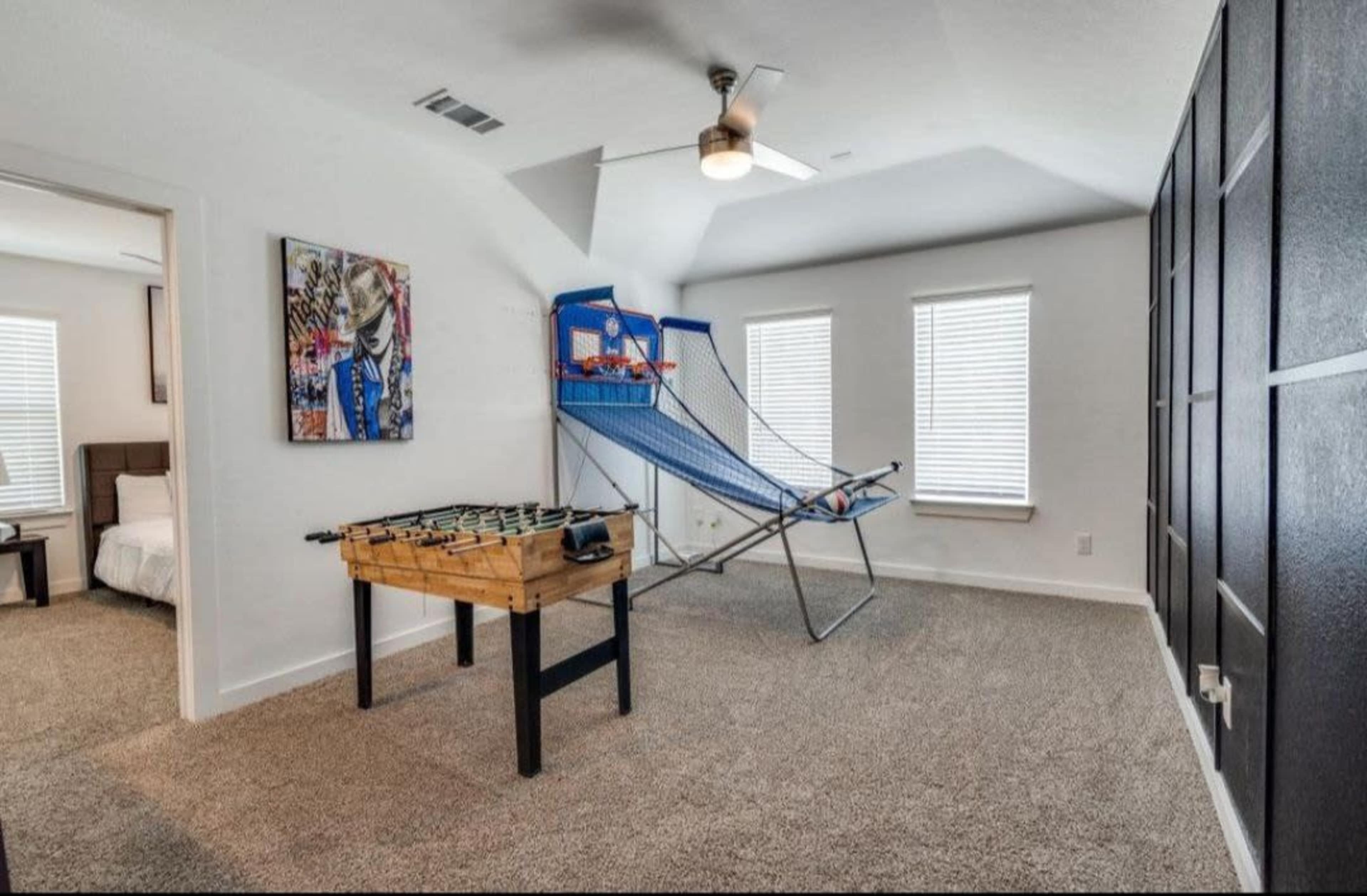 A game room featuring a foosball table and a basketball shooting game set against light-colored walls and windows.