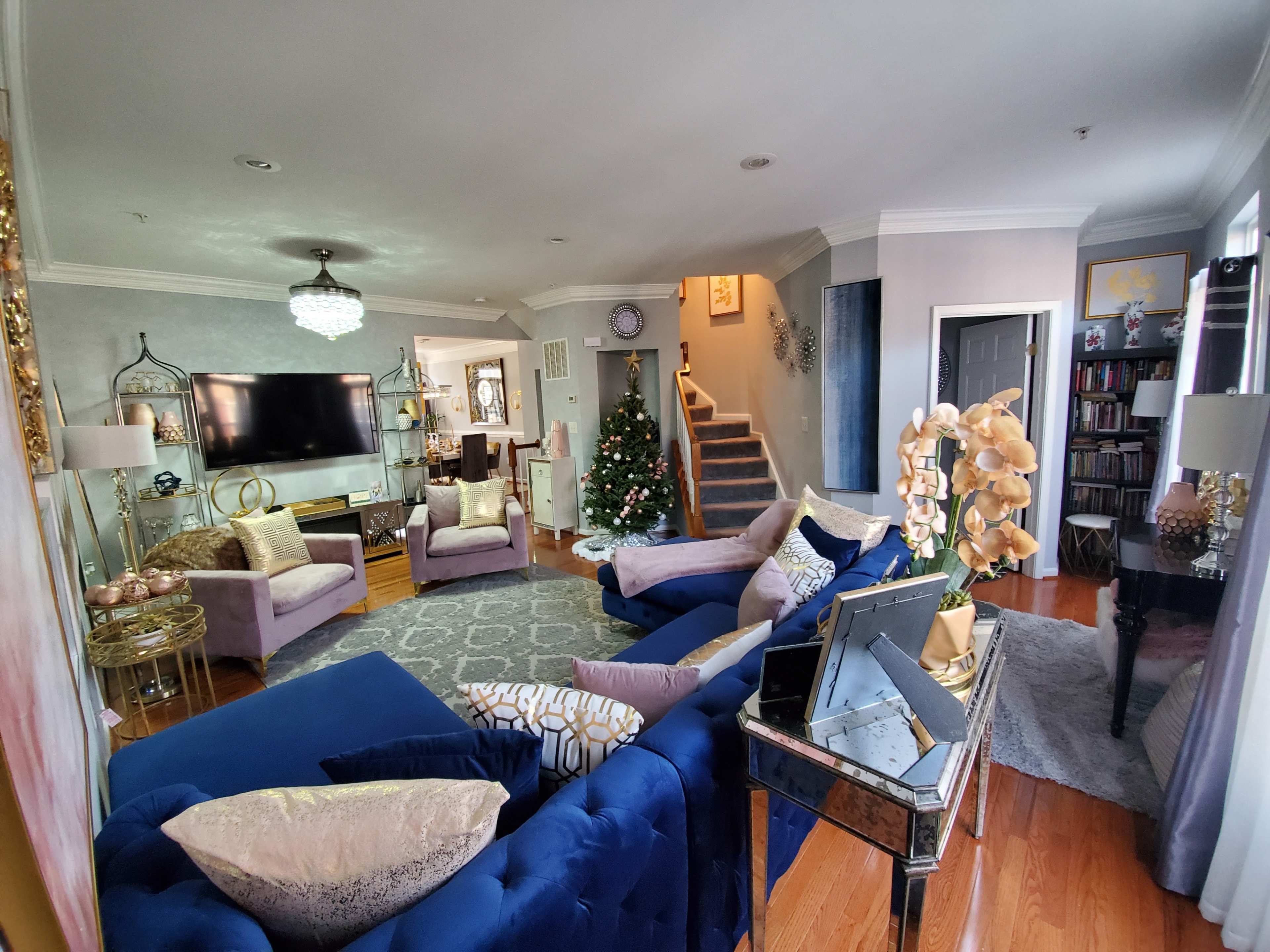 The living room features a blue sofa, purple chairs, a Christmas tree, and a staircase leading to an upper level.