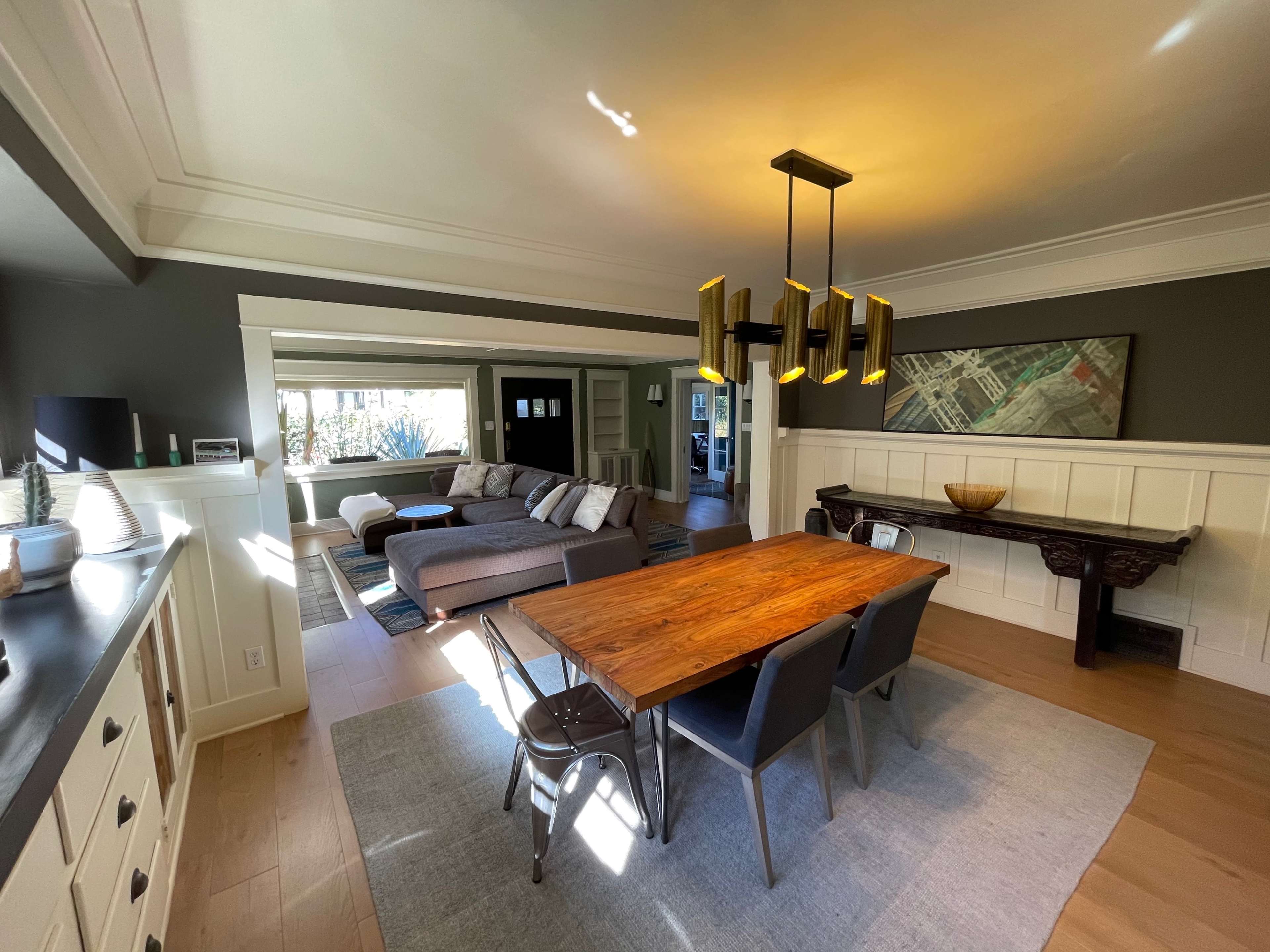 A modern dining area with a wooden table surrounded by chairs, overlooking a spacious living room featuring a sectional sofa and large windows.