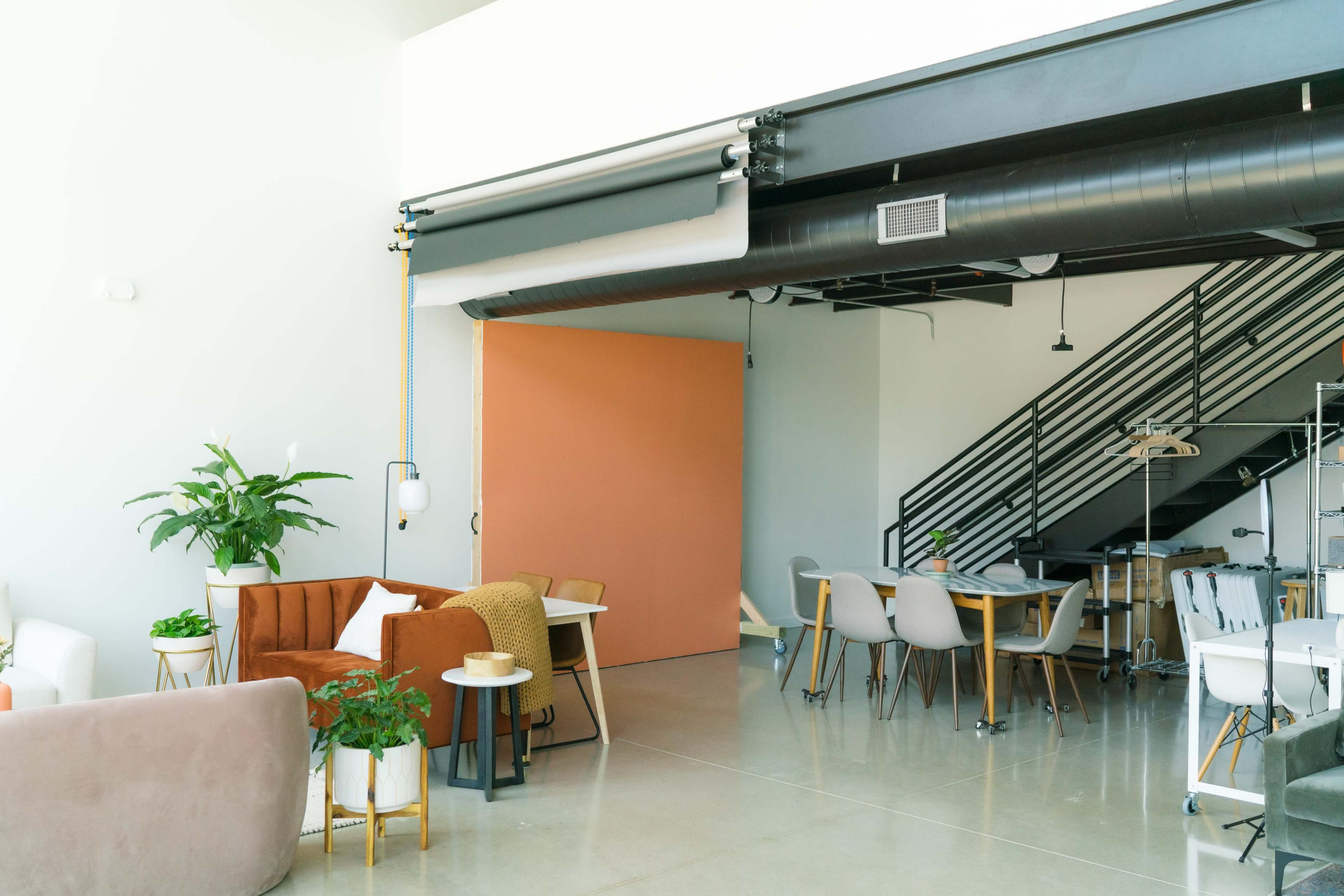A modern, open office space with a mix of seating areas, a staircase, and a large, orange sliding door.