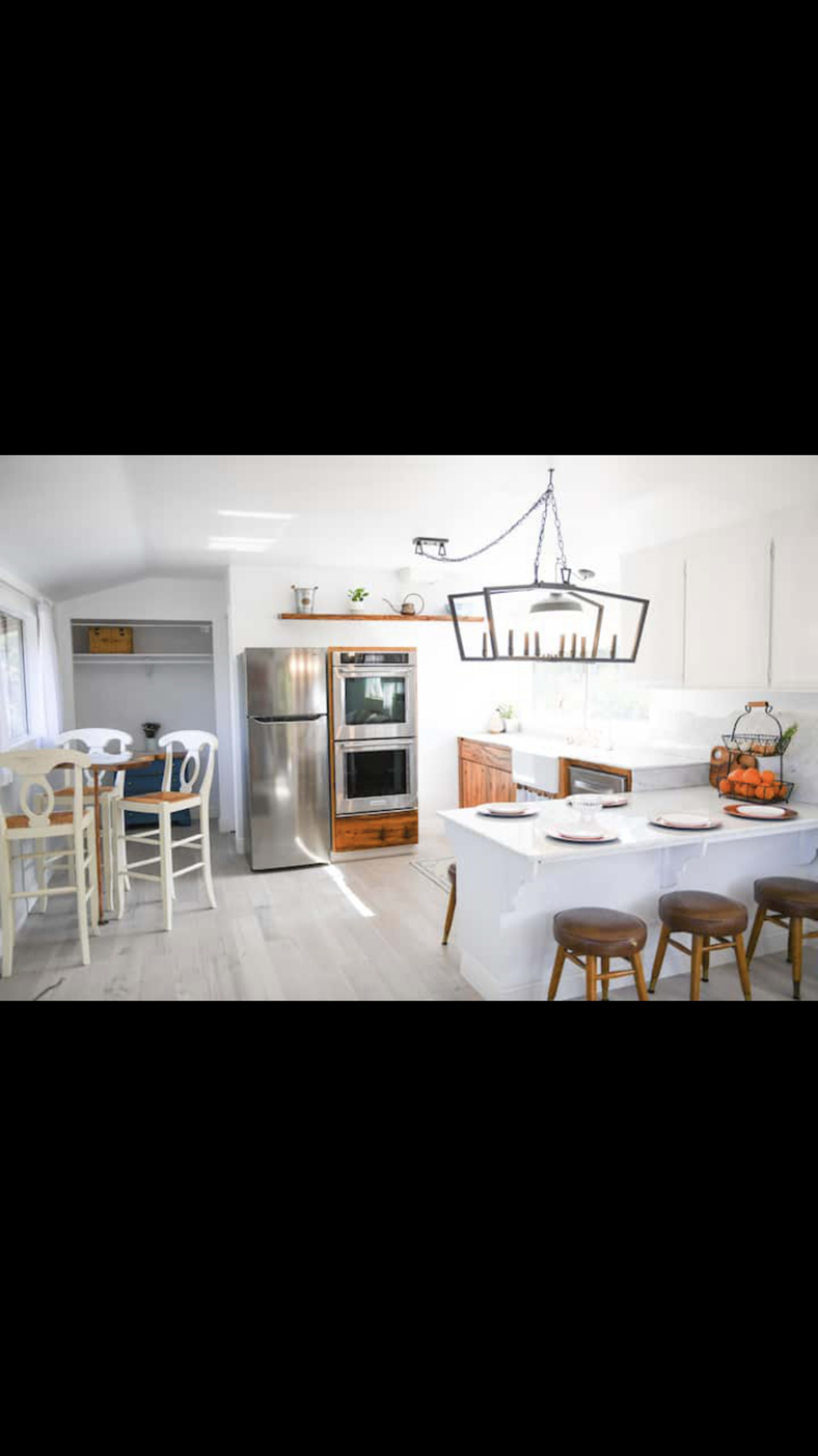 A modern kitchen with a stainless steel refrigerator, built-in oven, and a dining table with wooden stools.