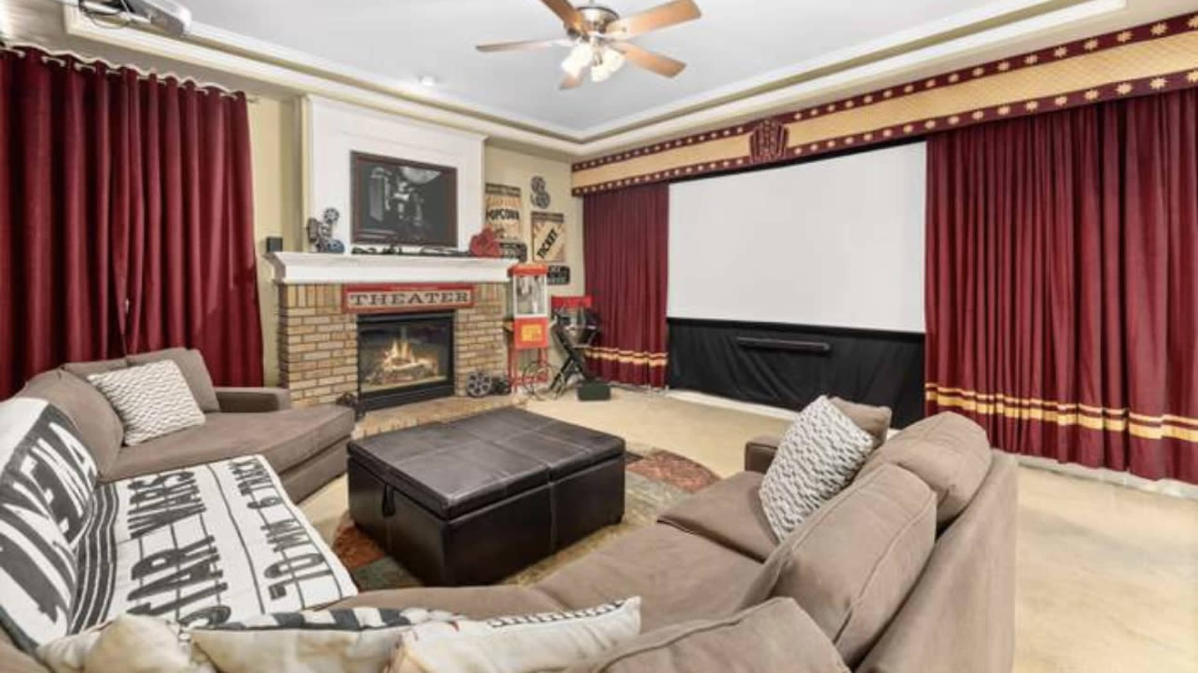 A home theater room featuring a large screen, comfortable seating, red curtains, and a fireplace with decorative elements.