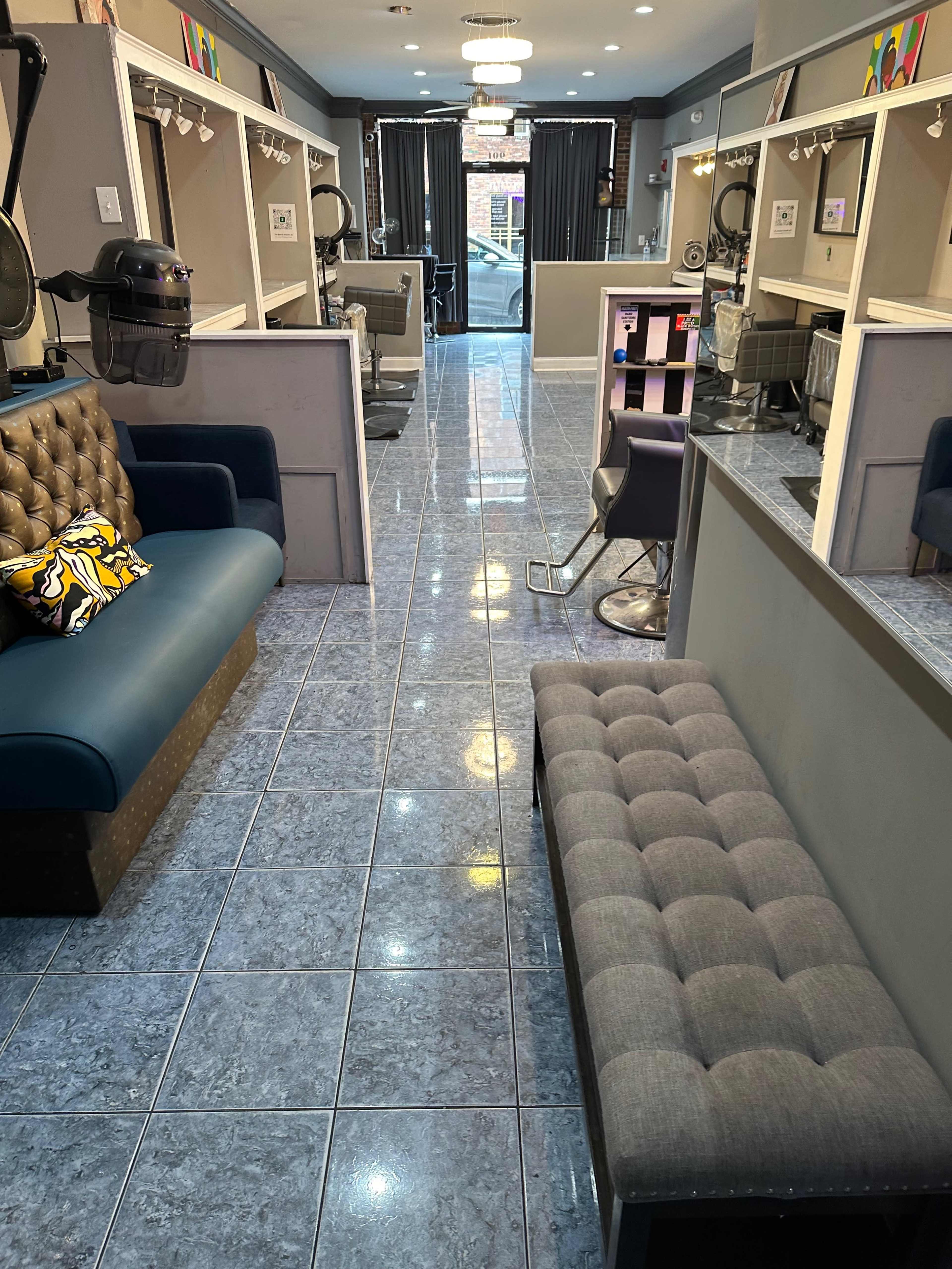 A hair salon interior featuring a row of styling stations, a waiting area with benches, and a glossy tiled floor.
