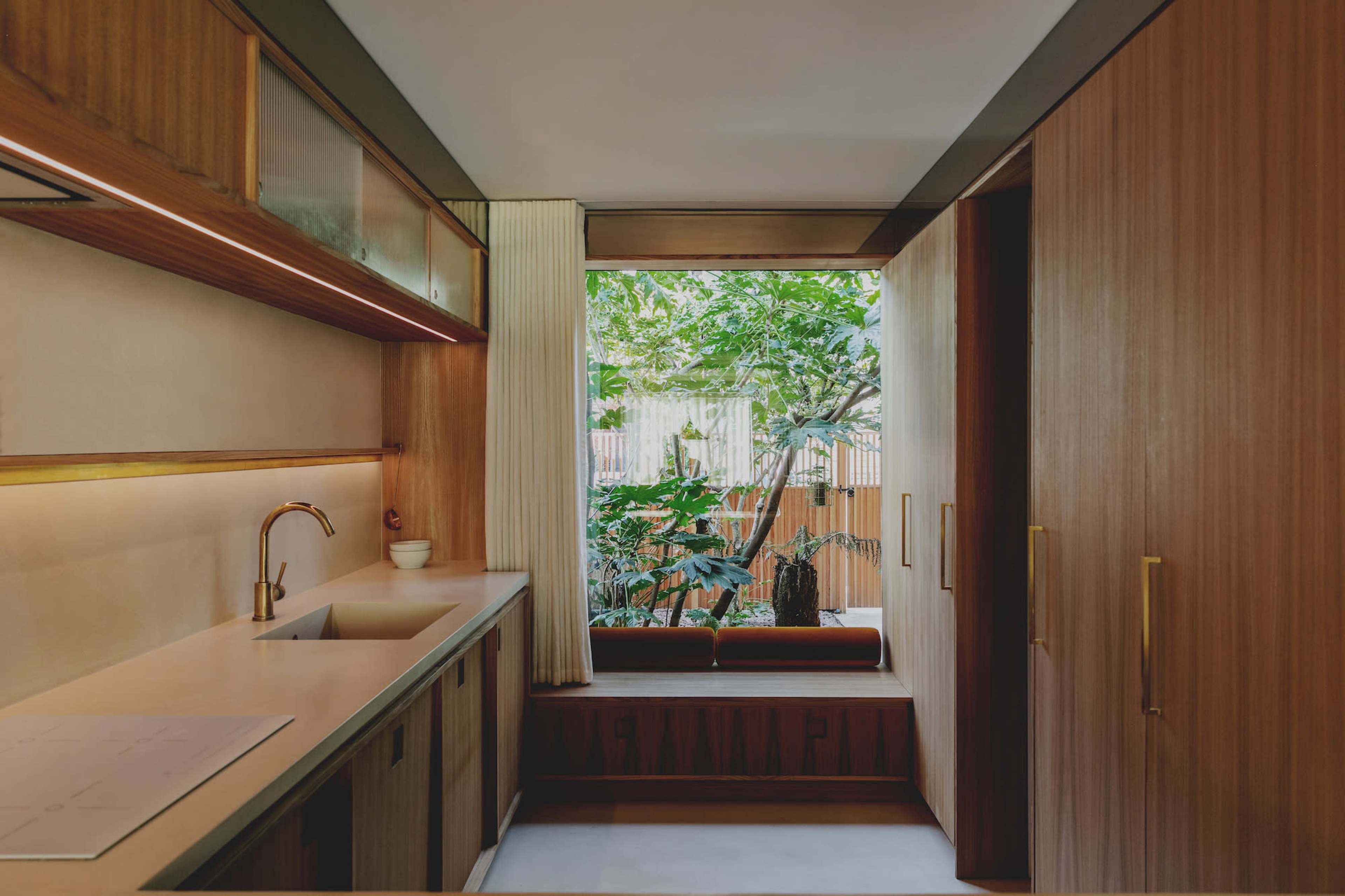 A modern kitchen features wooden cabinetry, a sink, and a window overlooking a green outdoor space.