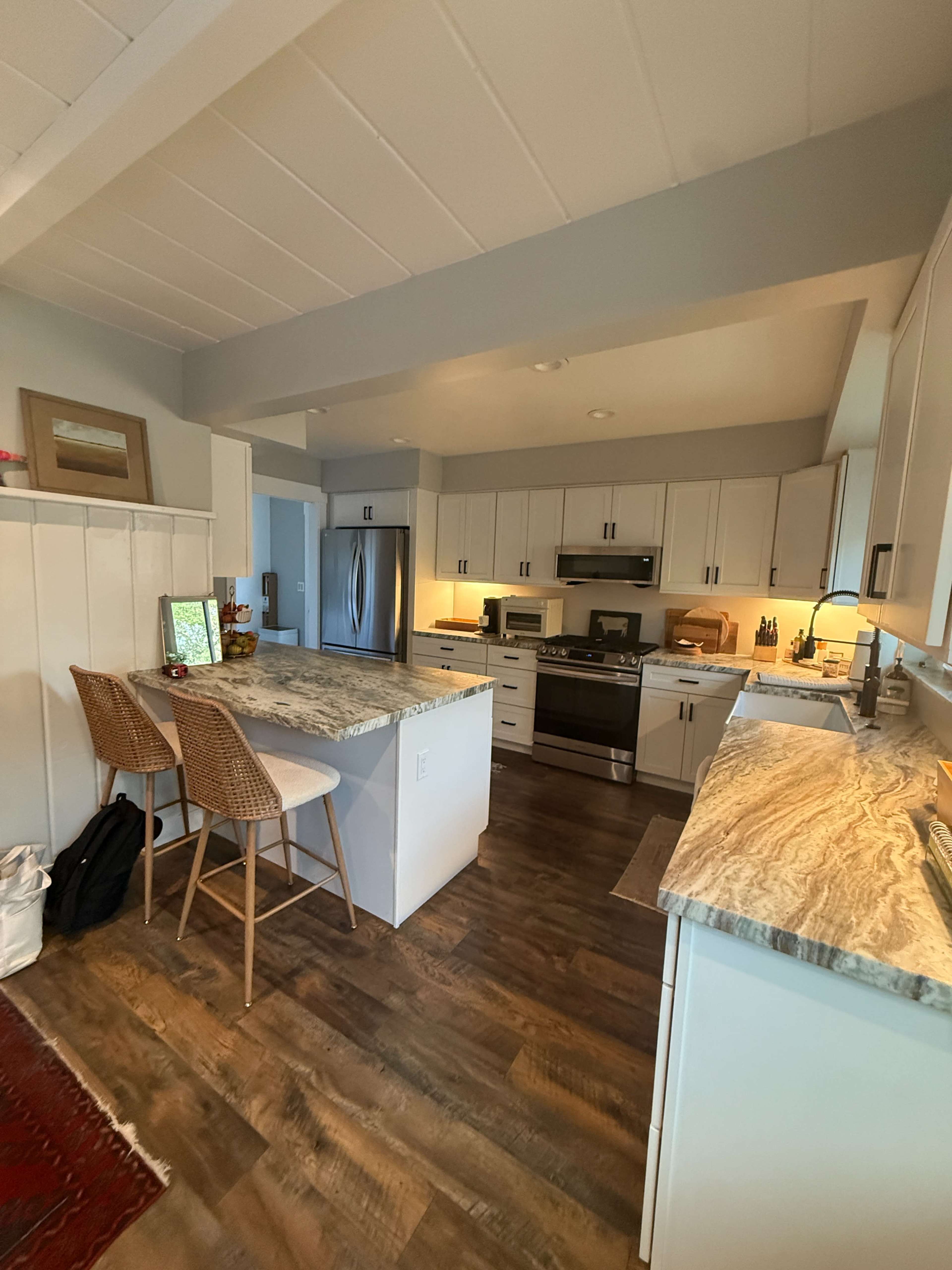 The image shows a modern kitchen featuring white cabinetry, a large central island with a marble countertop, and wooden flooring.