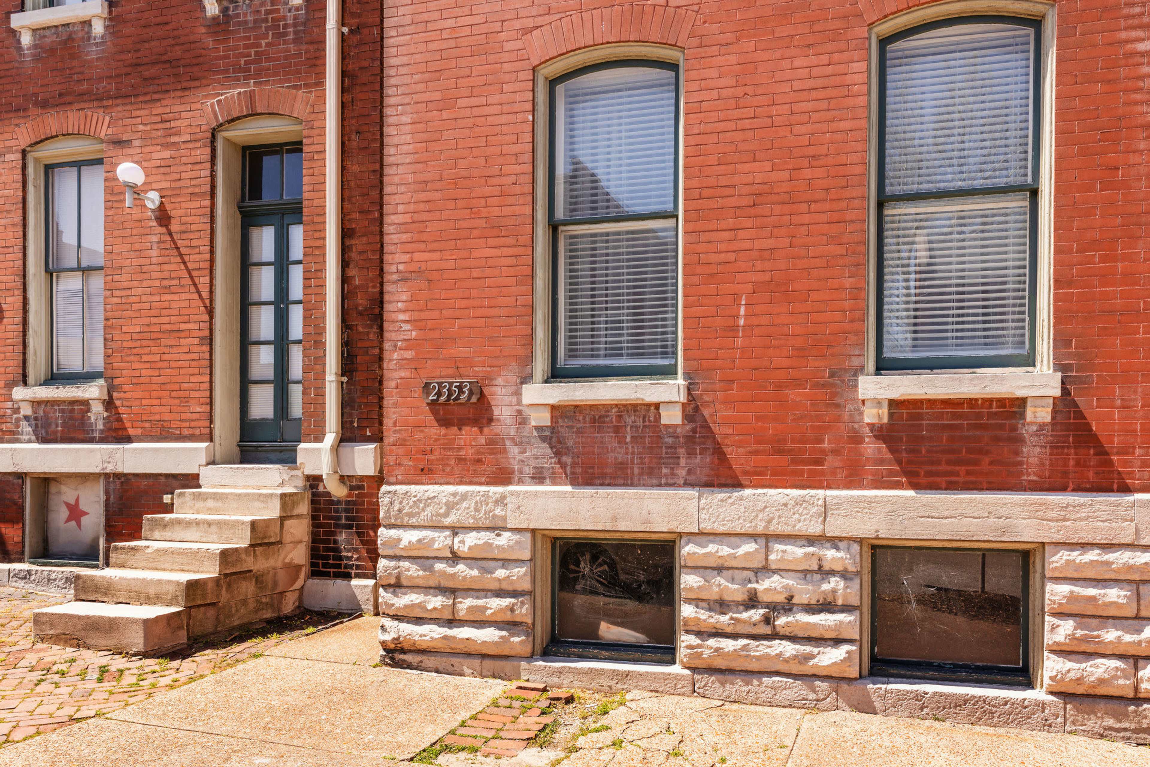 The image features a brick building with three windows and a set of steps leading to a door on the left side.